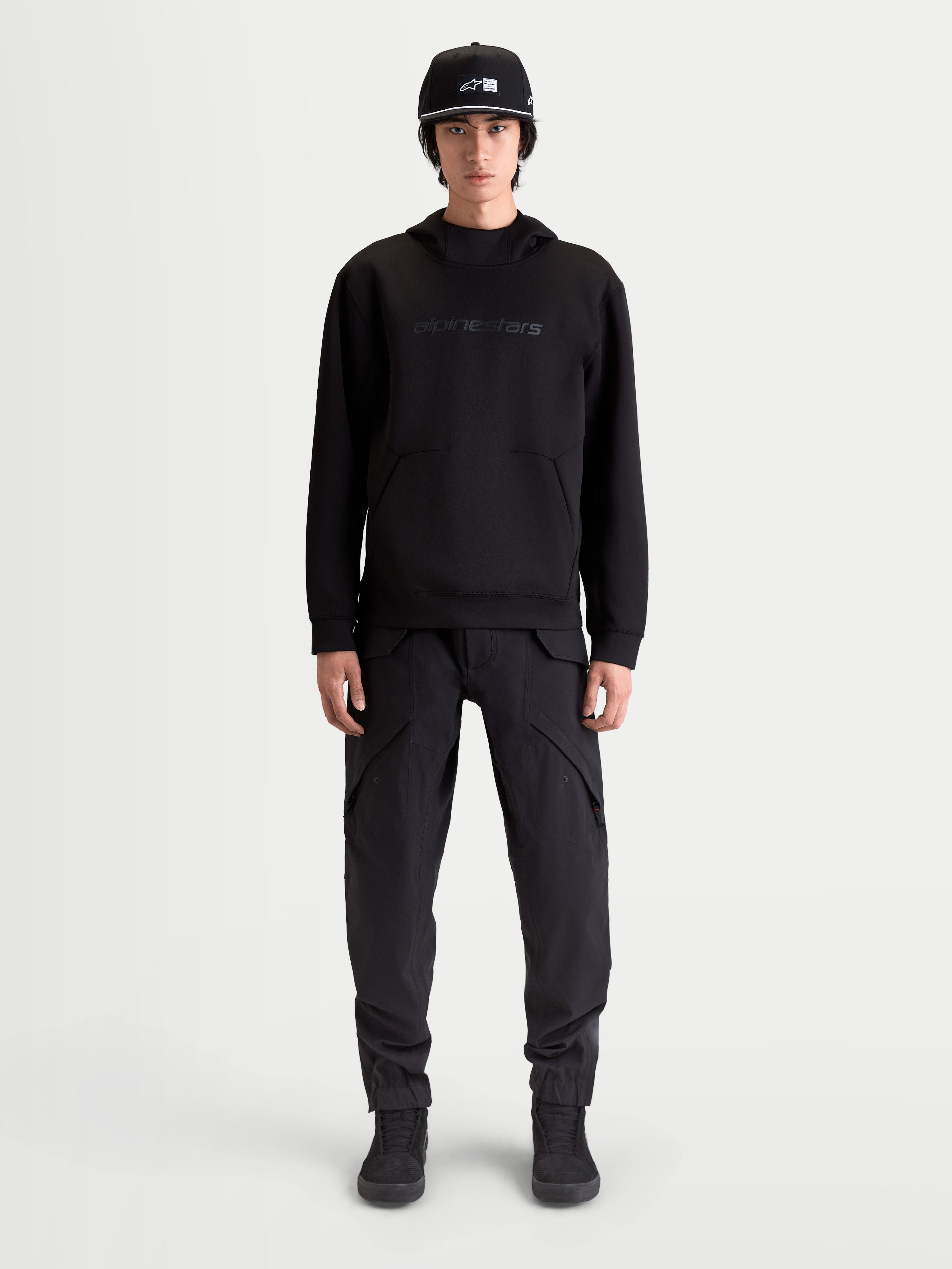 Alpinestars Sweat À Capuche Datrix, sweat à capuche sportswear pour homme, noir, avec marquage HD ton sur ton, polaire double face et poche avec détail de pli, porté par un modèle.