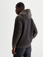 Alpinestars Sweat à capuche Infinite Washed Oversize, vêtement sportswear pour homme, noir délavé avec finition effet neige, polaire de coton, coupe décontractée, vue de dos sur modèle mettant en valeur le logo brodé sur la capuche et les détails côtelés.