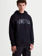 Alpinestars sweat à capuche Shaw Oversized, sweat à capuche de sportswear pour homme, noir, coupe ample et décontractée, logo texturé sur la poitrine, poche kangourou et capuche doublée, conçu en polaire de coton et polyester recyclé, vue de face sur modèle.
