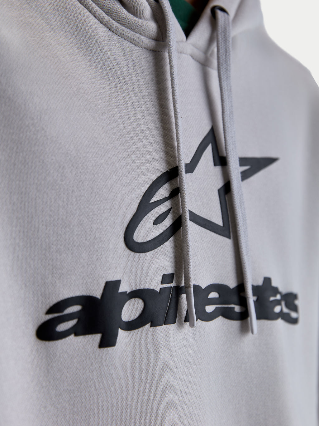 Alpinestars Prelude Oversized, sweat à capuche sportswear unisexe, gris ciment et noir, gros plan sur le logo et l'étoile en impression en relief, cordons de serrage plats