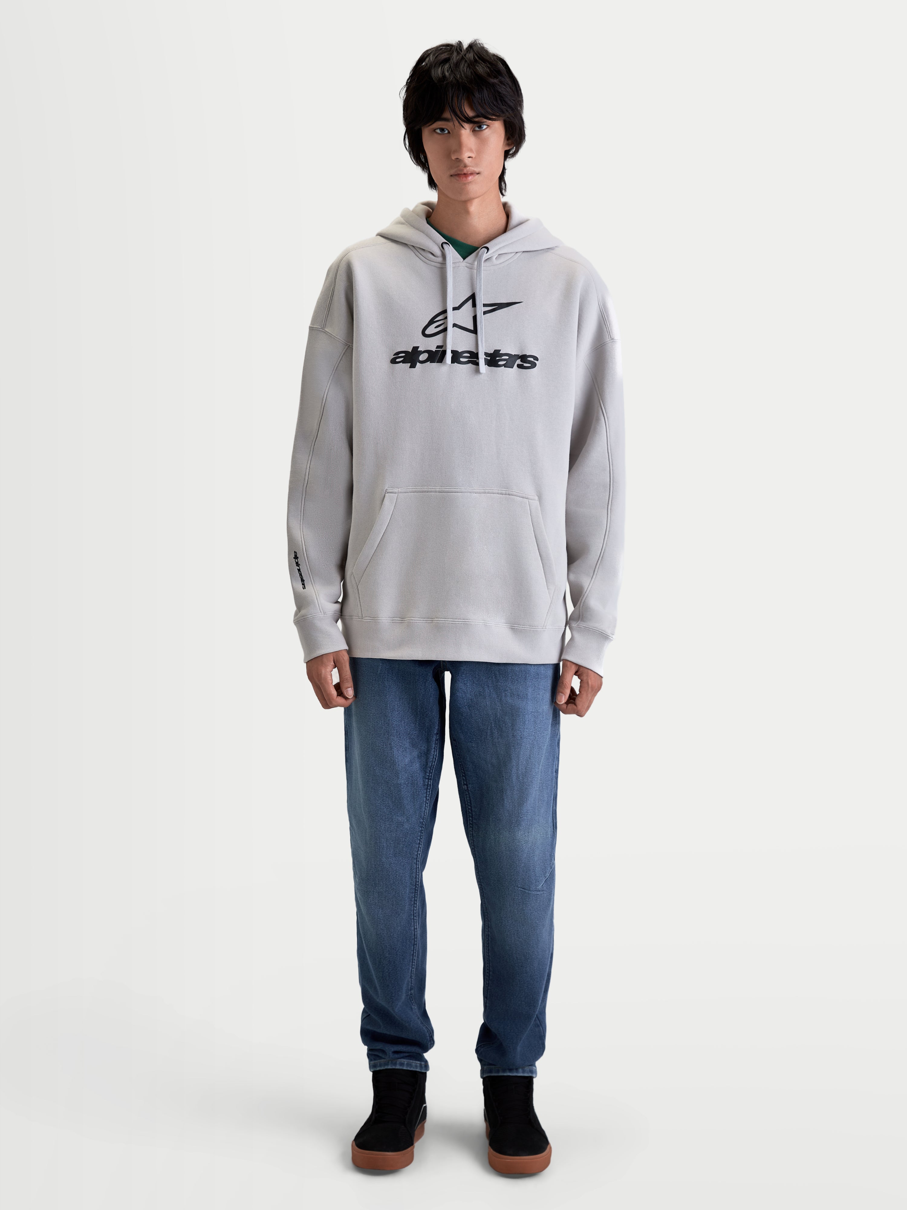 Alpinestars Prelude Oversized Hoodie, Men's Sportswear Fleece Pullover in Cement Gray. Features a relaxed fit with a black puff-print logo on the chest, a kangaroo pocket, and adjustable hood, shown on model with blue jeans.