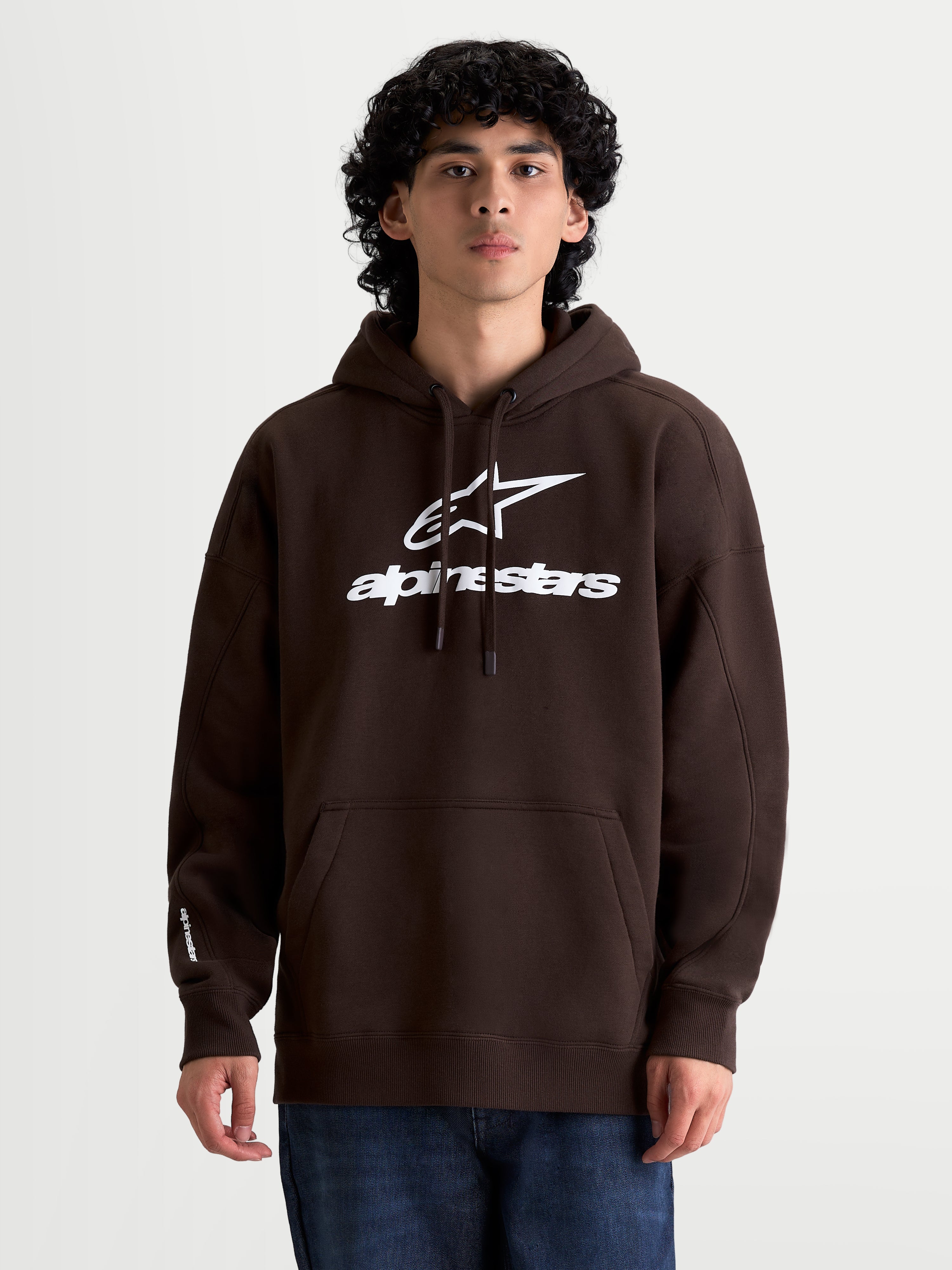 Alpinestars Prelude Oversized Hoodie on model, Men's Sportswear Fleece Pullover, Brown with White puff-print logo, oversized fit, kangaroo pocket, drawstring hood, cotton-rich blend.