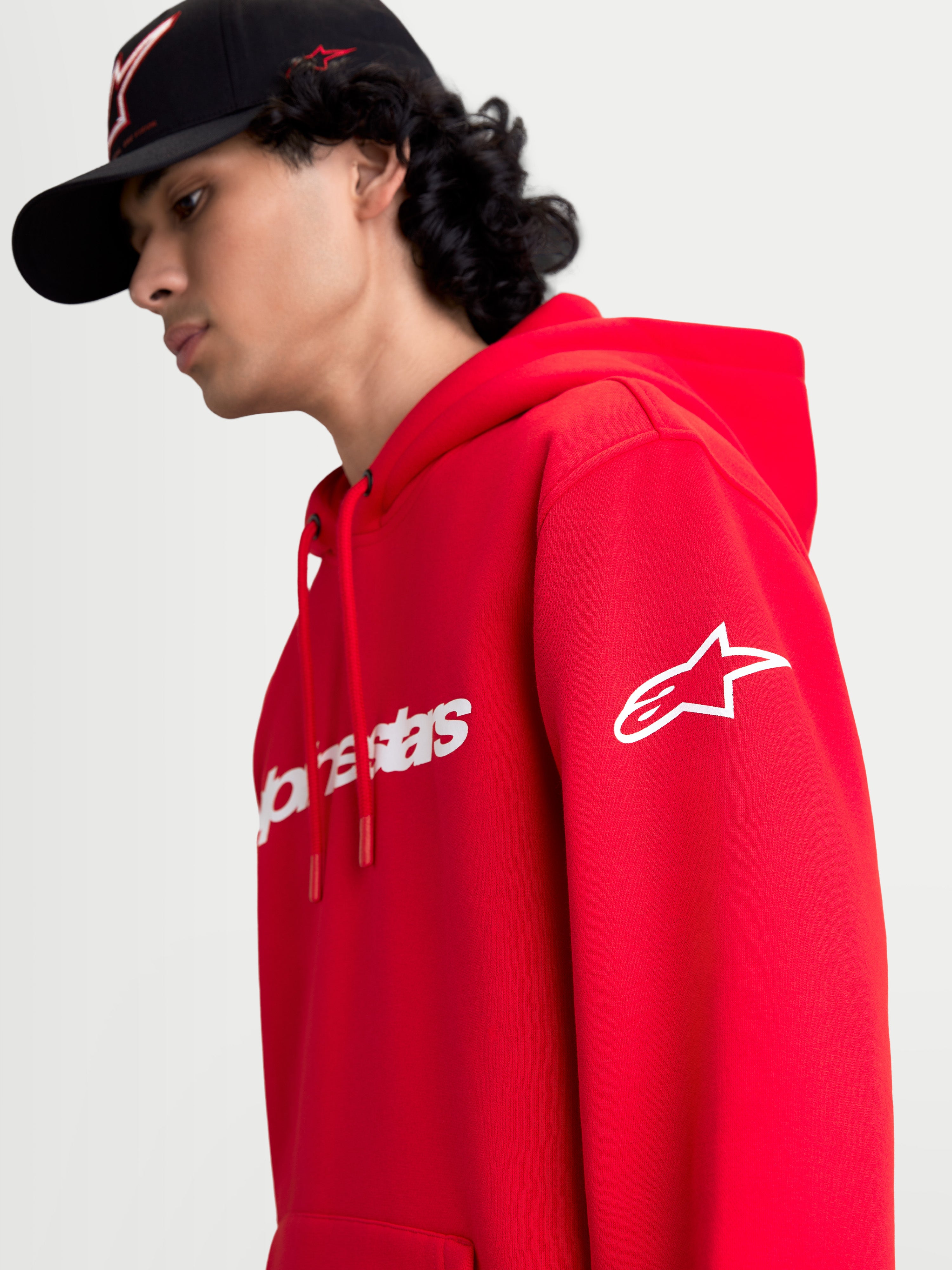 Alpinestars sweat à capuche Race Wordmark, pull en polaire de sportswear rouge et blanc, vue sur modèle présentant le logo Alpinestars Ageless blanc sur la manche et le marquage Race Linear à l'avant, design décontracté inspiré du sport automobile.