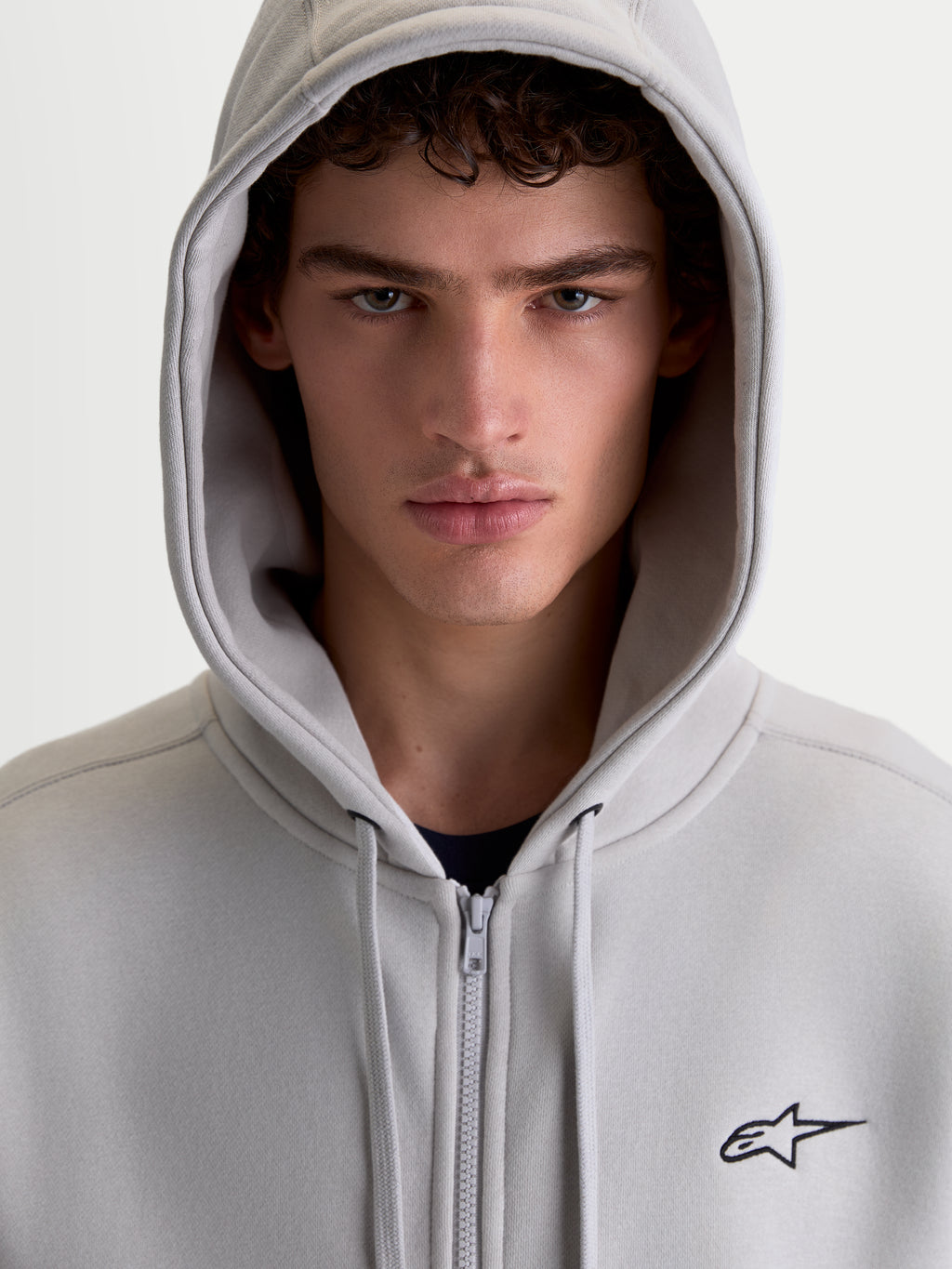 Alpinestars Sweat à capuche Entity Oversized, polaire sportswear zippée pour homme, gris, avec logo Astars noir brodé, portrait rapproché avec capuche relevée.