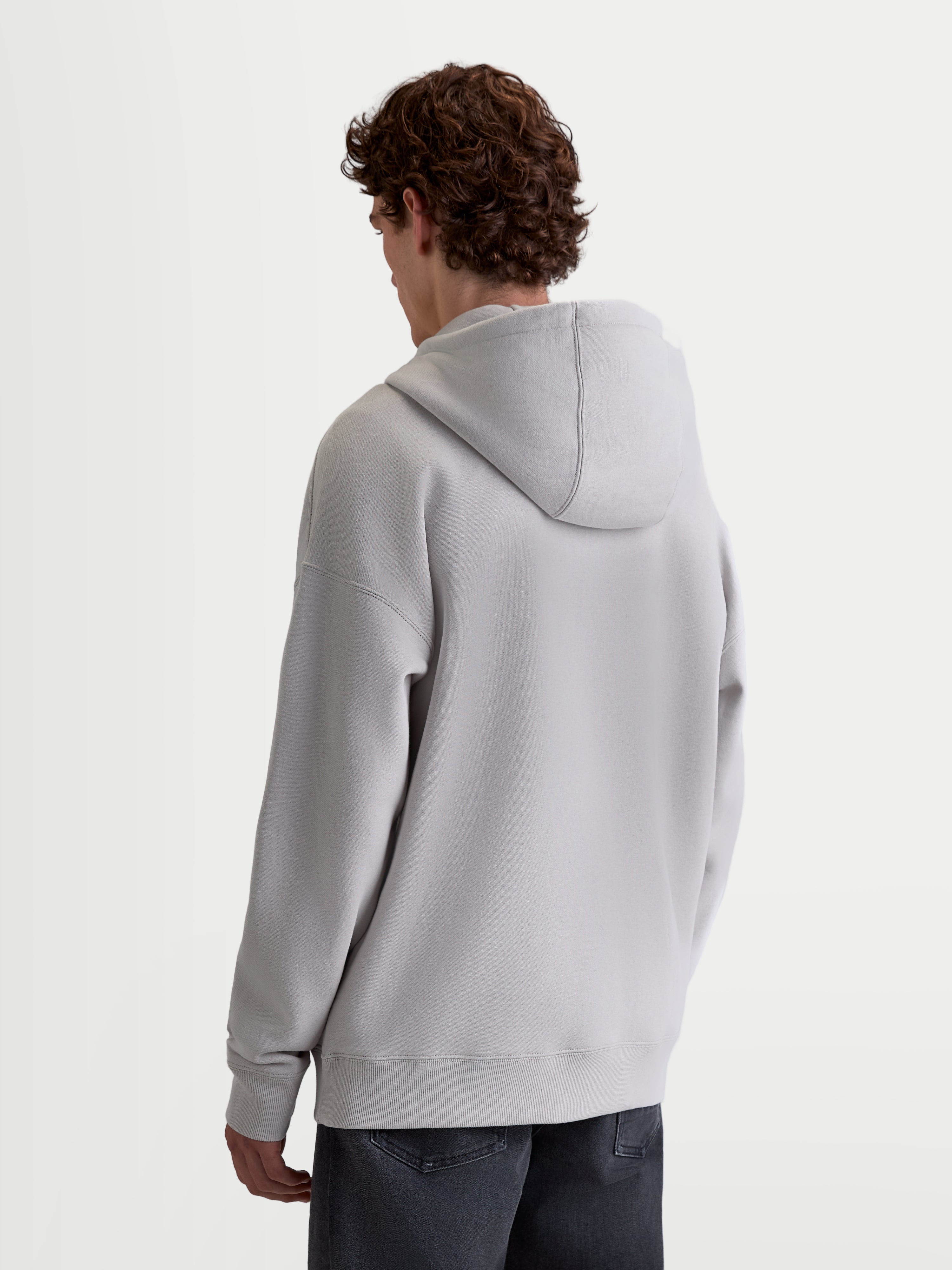 Alpinestars Sweat À Capuche Entity Oversized, sweat à capuche de sportswear pour homme et femme, vue de dos sur modèle, gris ciment, avec une coupe oversize décontractée, des épaules tombantes, une capuche doublée et des finitions côtelées.