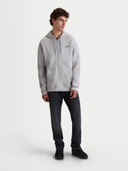 Alpinestars Sweat à capuche Entity Oversized, sweat à capuche sportswear unisexe en polaire gris ciment, coupe décontractée avec fermeture éclair frontale, poche kangourou et logo Astars brodé sur la poitrine, porté par un modèle pour un style lifestyle décontracté.
