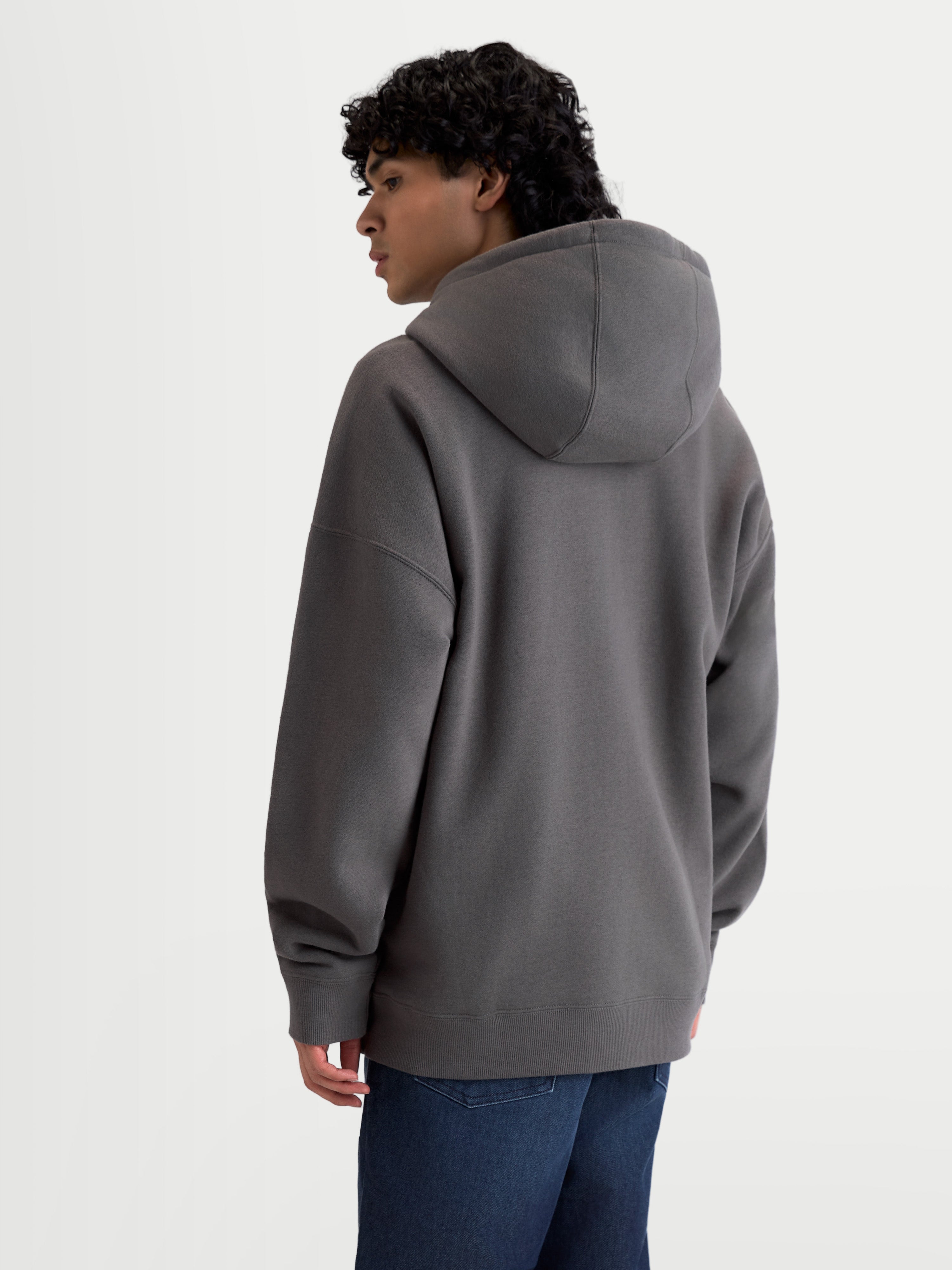 Alpinestars Sweat à capuche Entity Oversized, vêtement sportswear en polaire gris anthracite pour homme et femme, vue de dos sur mannequin montrant une silhouette décontractée et un ourlet côtelé.