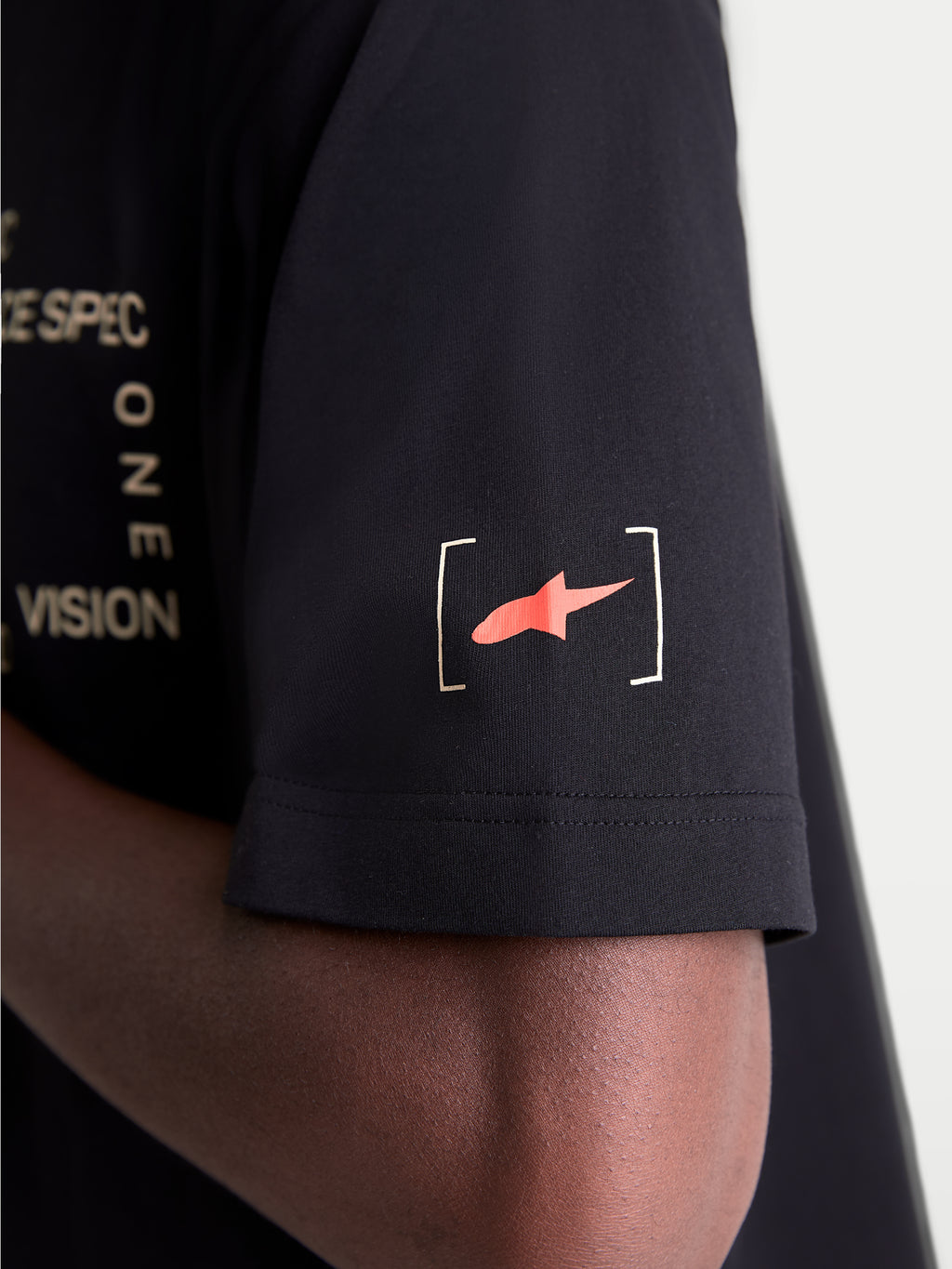 Alpinestars Infinity Oversized CSF, t-shirt sportswear à manches courtes noir, vue rapprochée de la manche avec le logo Astars rouge entre crochets et marquages blancs, vêtement décontracté pour homme et femme.