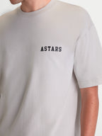 Alpinestars T-Shirt Latitude Oversized CSF, t-shirt de sportswear à manches courtes, gris ciment avec logo ASTARS noir sur la poitrine, coupe décontractée oversize, porté par un modèle.