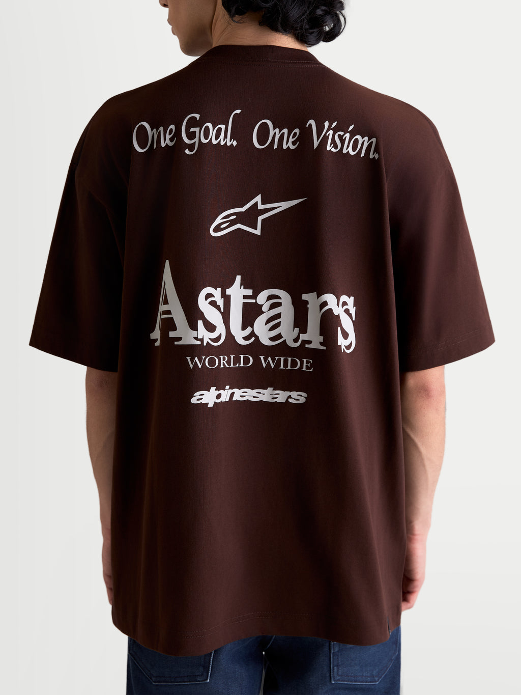 Alpinestars T-Shirt Post Oversized CSF, t-shirt sportswear à manches courtes, marron et blanc, vue de dos sur modèle avec graphismes blancs One Goal. One Vision. et Astars World Wide, coupe oversize décontractée en mélange coton et polyester.