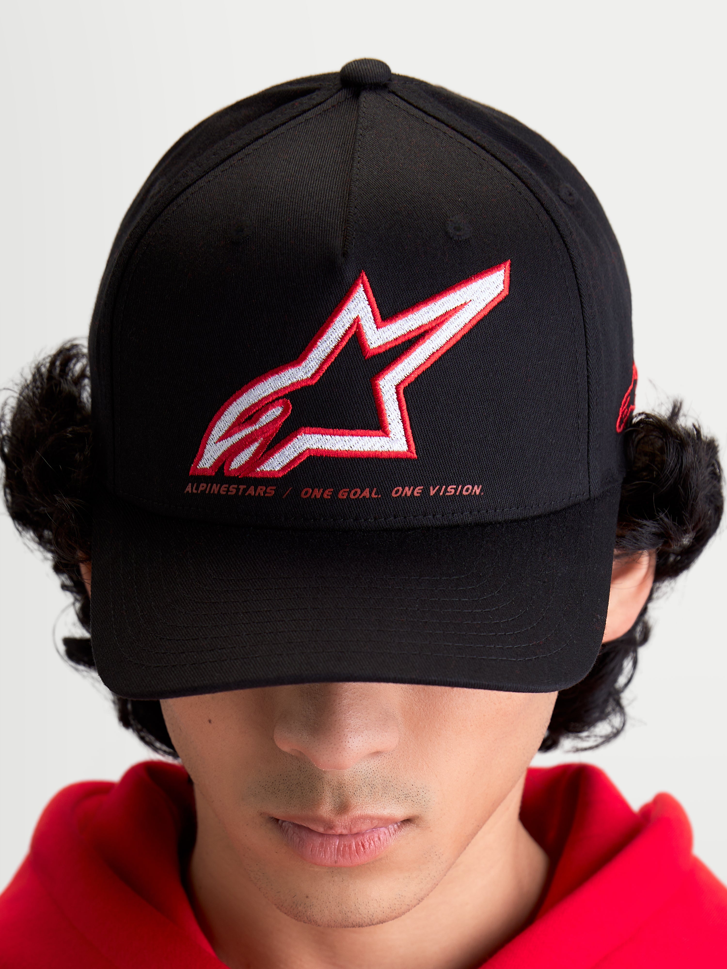 Alpinestars casquette Lineout, casquette de sportswear pour homme et femme, noire avec logo Astars brodé en rouge et blanc et slogan One Goal One Vision, visière incurvée, couronne structurée, construction en textile, portée par un modèle