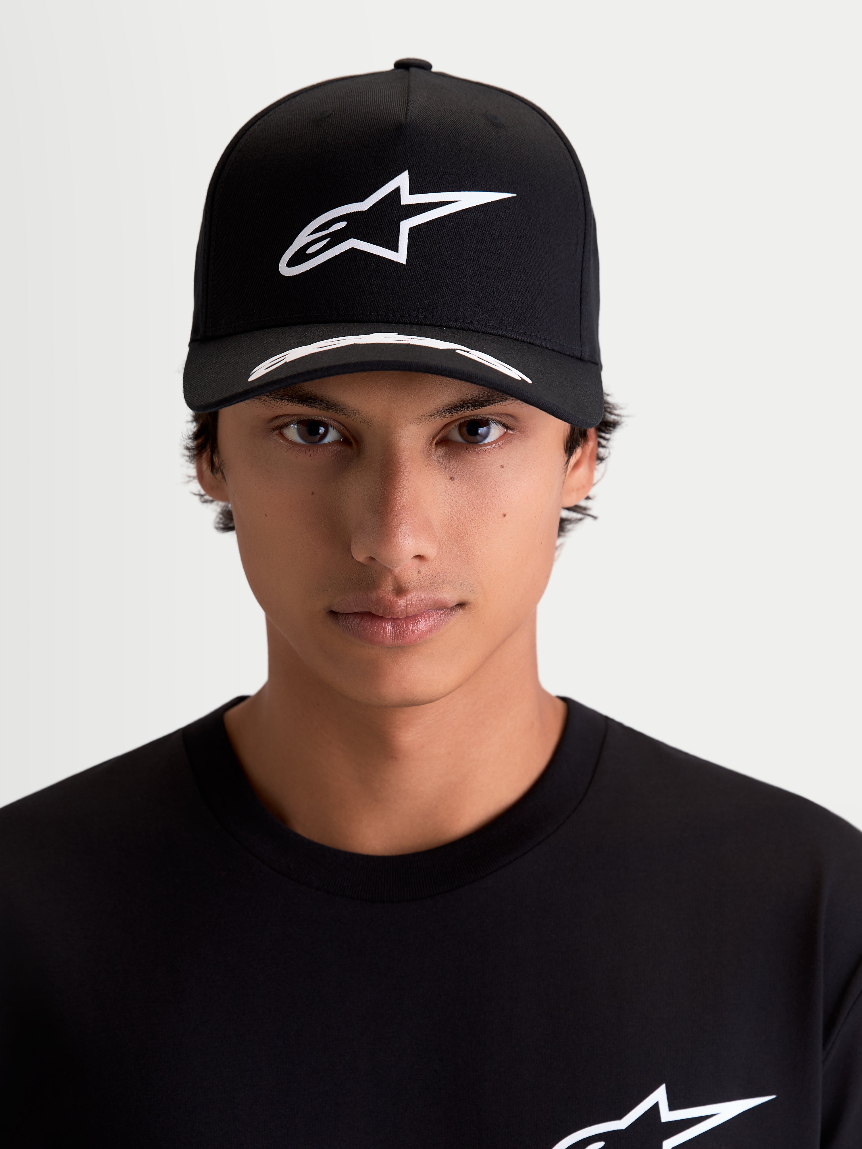 Alpinestars Arclight, casquette de sportswear noire et blanche, vue de face sur modèle. Comprend un logo Astars blanc en relief sur une couronne structurée, une visière incurvée avec détails et un tissu en sergé premium.