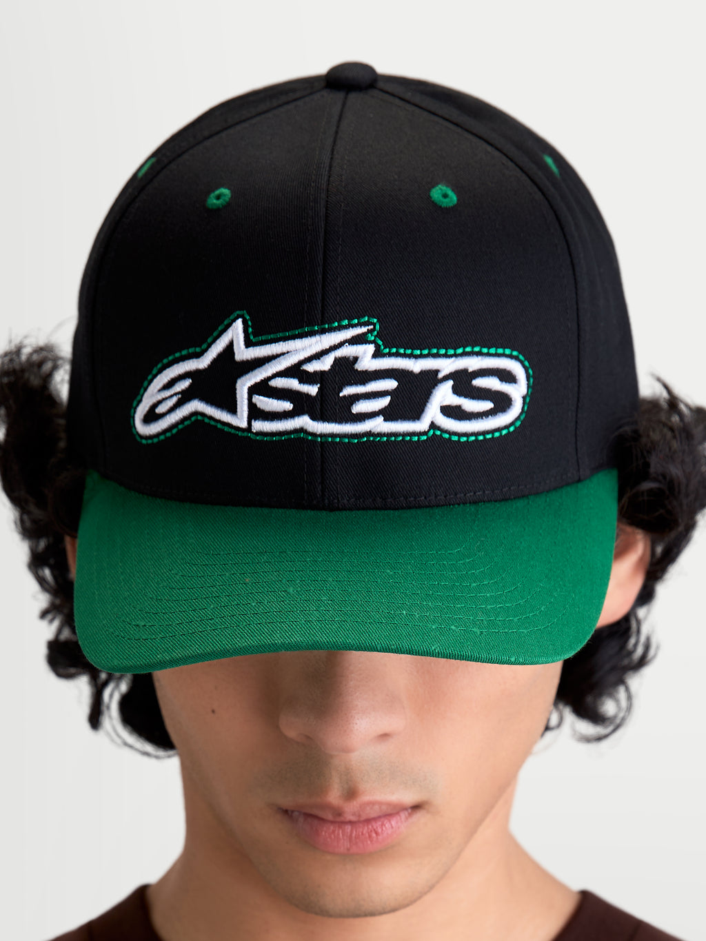 Alpinestars Casquette Retro Snapback, casquette de sportswear d'inspiration motorsport, unisexe, noire et verte, en sergé de coton, visière incurvée et couronne structurée, vue de face sur modèle avec logo Astars et surpiqûres vertes.