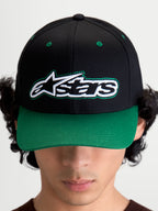 Alpinestars Casquette Retro Snapback, casquette de sportswear d'inspiration motorsport, unisexe, noire et verte, en sergé de coton, visière incurvée et couronne structurée, vue de face sur modèle avec logo Astars et surpiqûres vertes.
