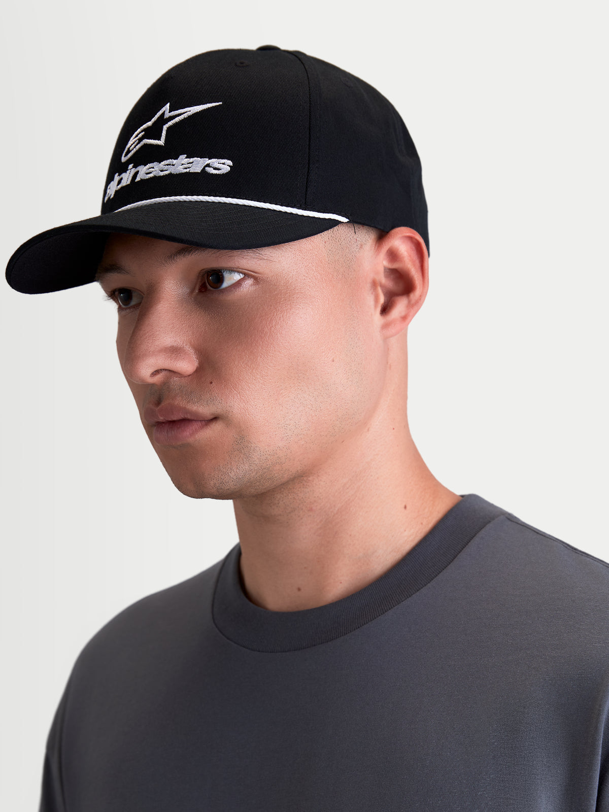 Alpinestars Combo Logo Snapback, casquette de sportswear noire et blanche, visière courbée et couronne structurée, broderie logo Alpinestars combo blanc avec détail de cordelette, vue de profil sur modèle.