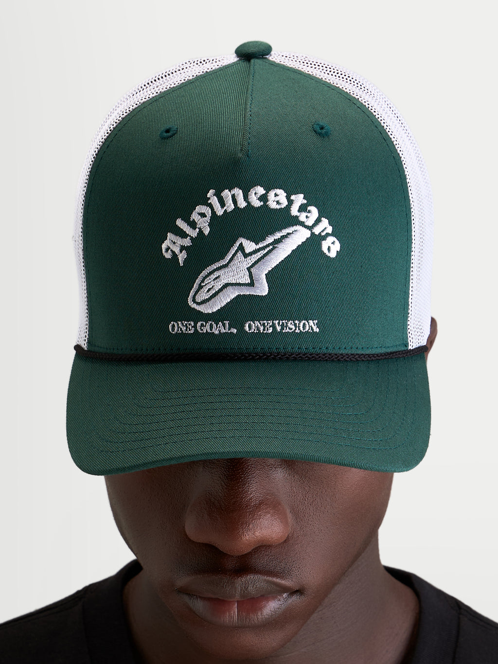 Alpinestars Casquette Baron Trucker, casquette sportswear verte et blanche, portée par un modèle, avec visière courbée, panneau avant structuré et logo brodé sur l'avant
