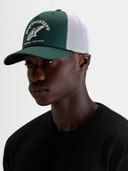 Alpinestars Casquette Baron Trucker, casquette sportswear verte et blanche portée par un modèle, avec visière courbée, couronne structurée en sergé, dos en maille respirante et logo brodé sur l'avant