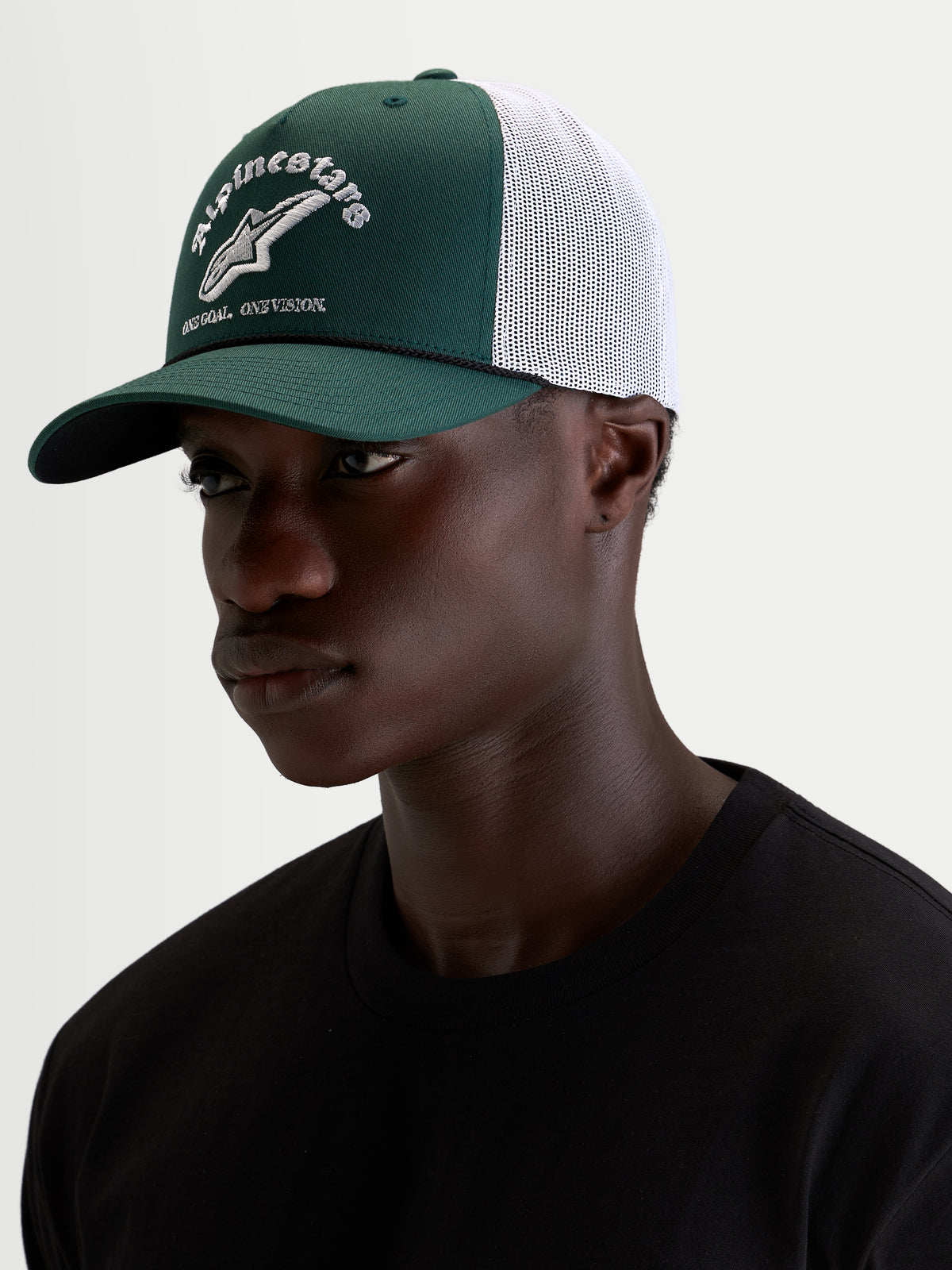 Alpinestars Casquette Baron Trucker, casquette sportswear verte et blanche portée par un modèle, avec visière courbée, couronne structurée en sergé, dos en maille respirante et logo brodé sur l'avant
