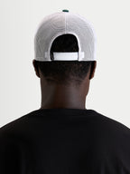 Casquette Baron Trucker d'Alpinestars, casquette trucker sportswear, portée par un modèle, vue de dos montrant la fermeture snapback réglable, les panneaux arrière en maille polyester blanche et le bouton de couronne vert
