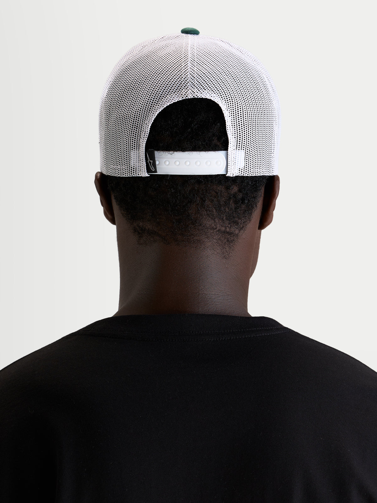 Casquette Baron Trucker d'Alpinestars, casquette trucker sportswear, portée par un modèle, vue de dos montrant la fermeture snapback réglable, les panneaux arrière en maille polyester blanche et le bouton de couronne vert