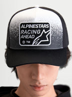Alpinestars Casquette Trucker Gravel, casquette sportswear unisexe, noire et blanche, avec écusson tissé Alpinestars Racing Ahead à texture gravier, couronne structurée et visière courbée, vue de face sur modèle