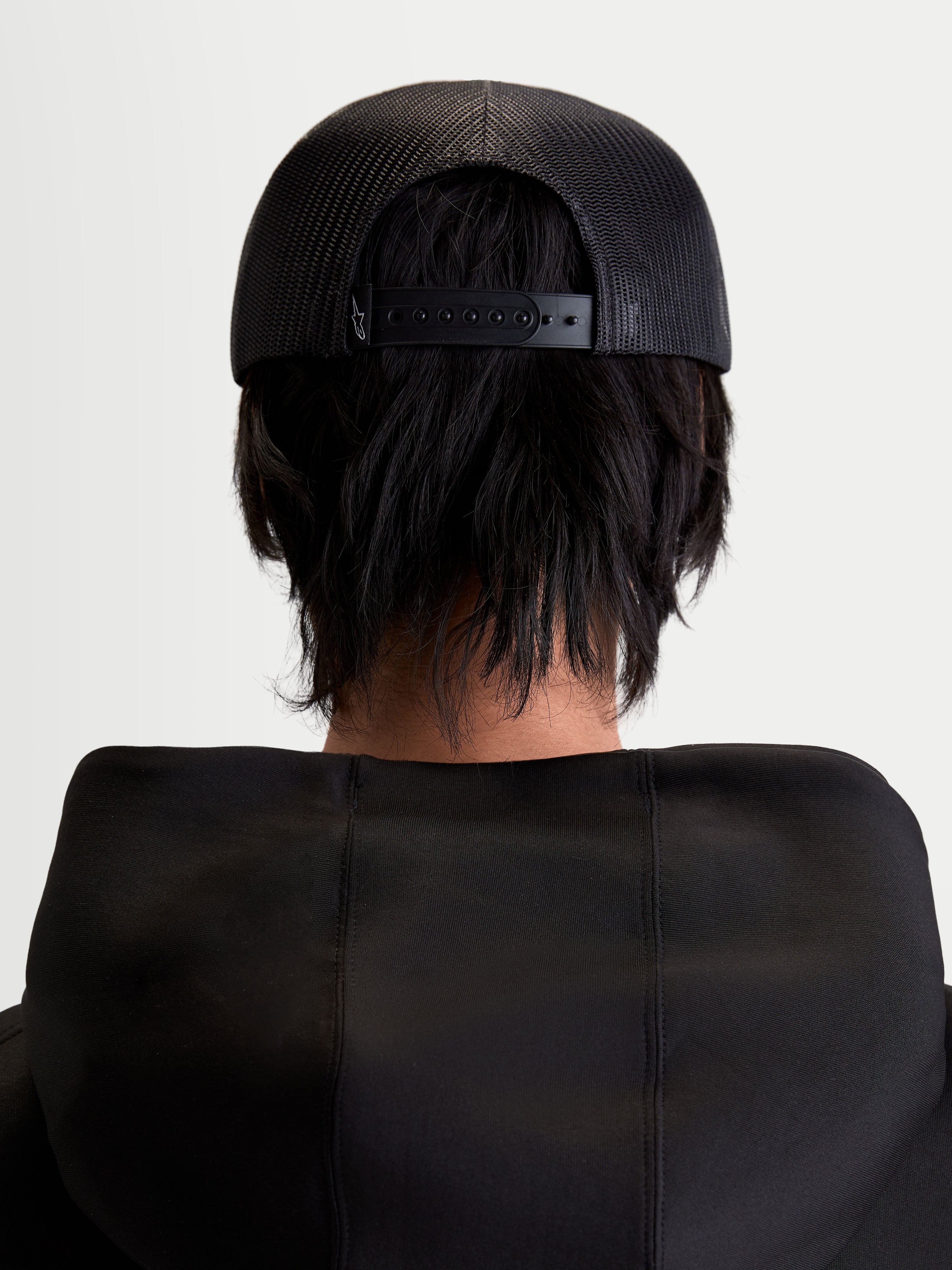 Alpinestars Casquette Trucker Gravel, casquette sportswear noire, vue de dos sur modèle montrant l'arrière en maille polyester respirante et la fermeture à pression réglable, style décontracté unisexe