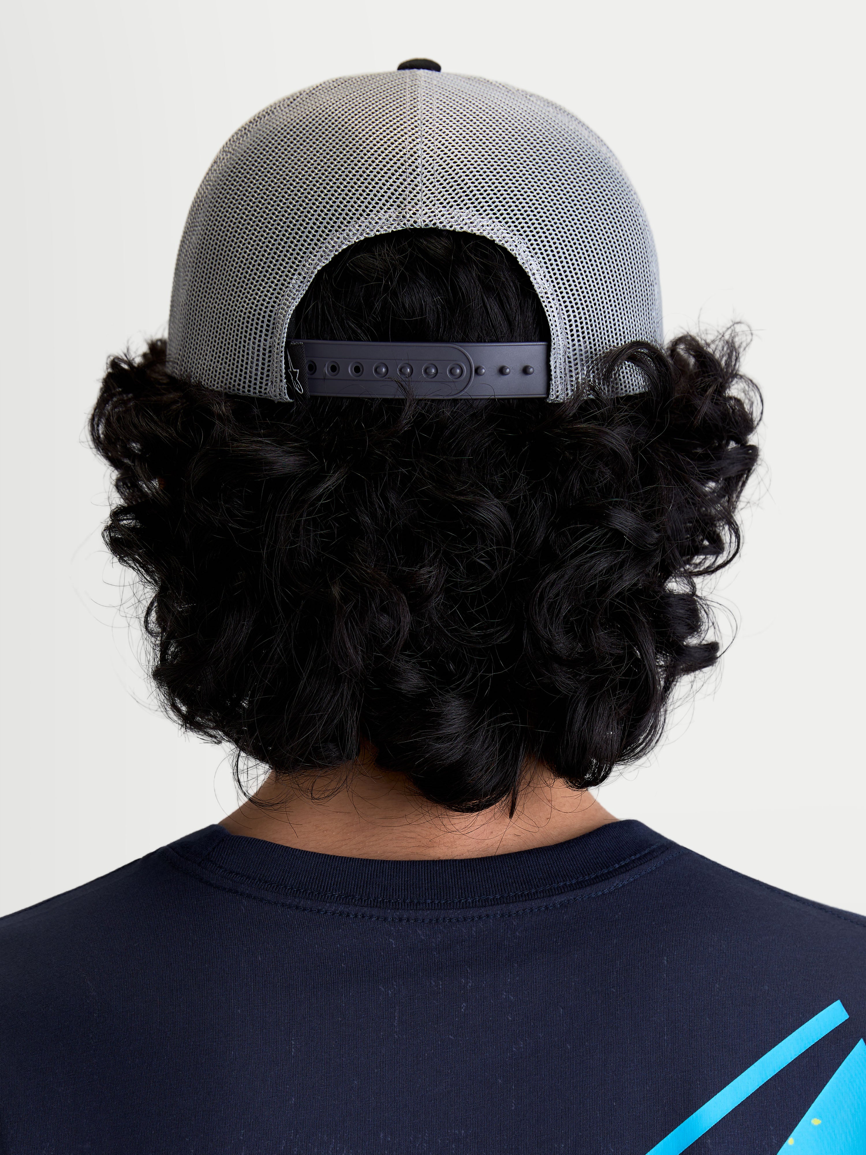 Alpinestars Gravel, casquette trucker sportswear grise et noire, vue de dos sur un modèle montrant l'arrière en maille polyester respirante et la fermeture à pression réglable pour un ajustement personnalisé