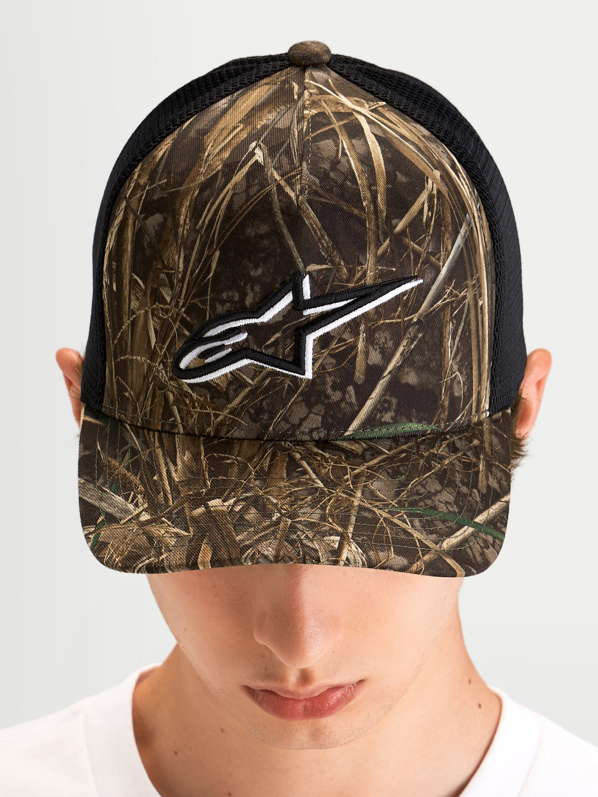 Casquette Trucker Thicket Realtree d'Alpinestars, casquette trucker sportswear portée par un modèle, camouflage Realtree et noir, visière courbée, couronne structurée et logo Astars brodé blanc sur le devant