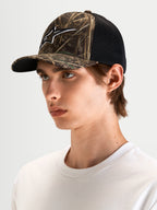 Alpinestars Casquette Trucker Thicket Realtree, casquette sportswear camouflage et noire, visière courbée, couronne structurée et logo Astars brodé en 3D, portée par un modèle