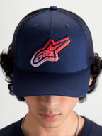 Alpinestars Casquette Trucker Meteorite, casquette de sportswear pour homme et femme, bleu marine avec écusson logo Astars rouge et blanc à texture gravier, couronne structurée et visière incurvée, vue de face portée
