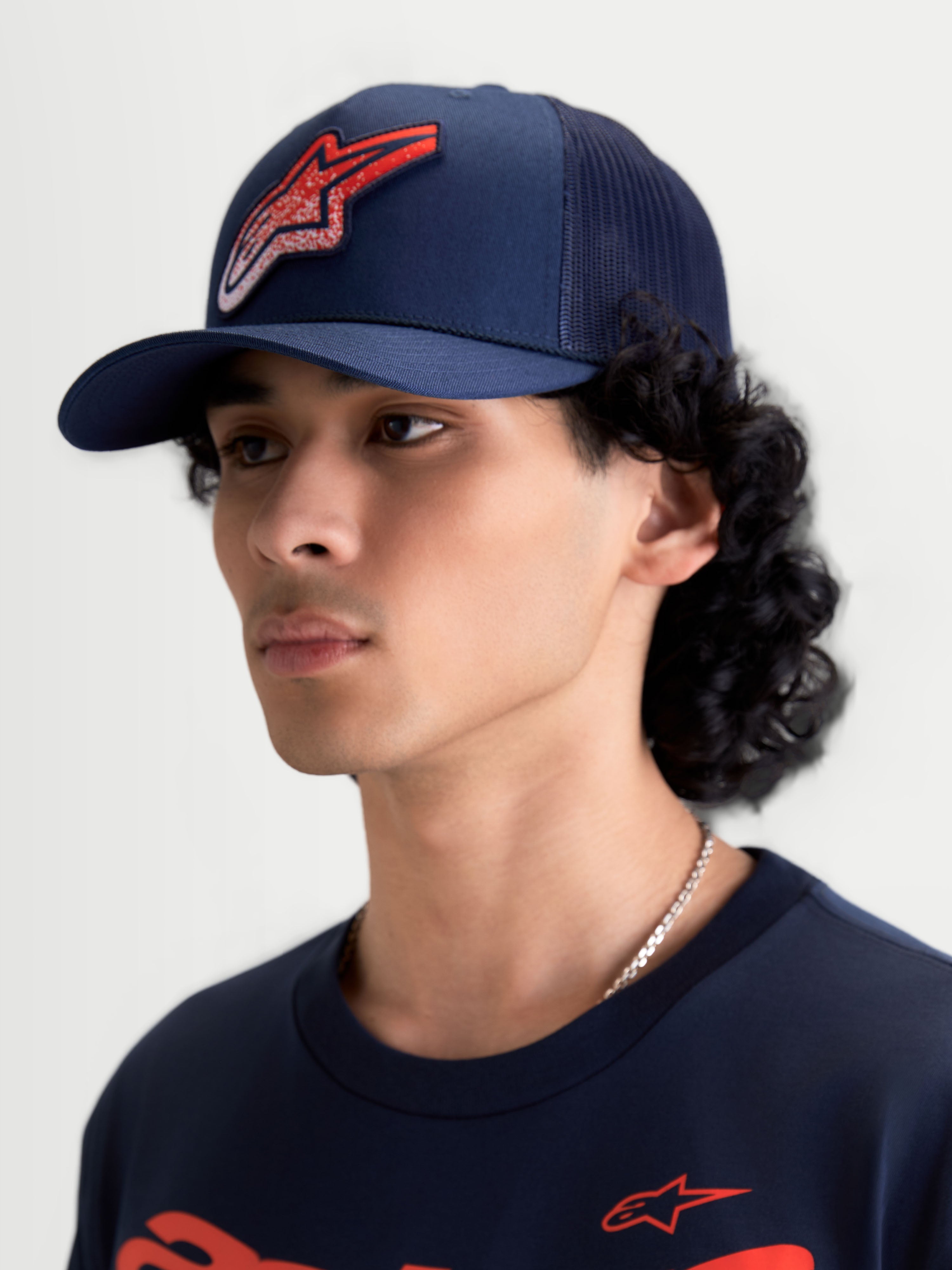 Alpinestars casquette Trucker Meteorite, casquette de sportswear avec arrière en maille, bleu marine et rouge, visière incurvée et couronne structurée, logo Astars à texture gravier, vue portée par un modèle