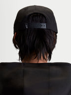 Alpinestars Casquette Label Snapback, casquette de sportswear noire pour homme et femme, vue de dos sur modèle montrant la fermeture snapback réglable avec un petit logo blanc, construction en sergé de coton structuré.