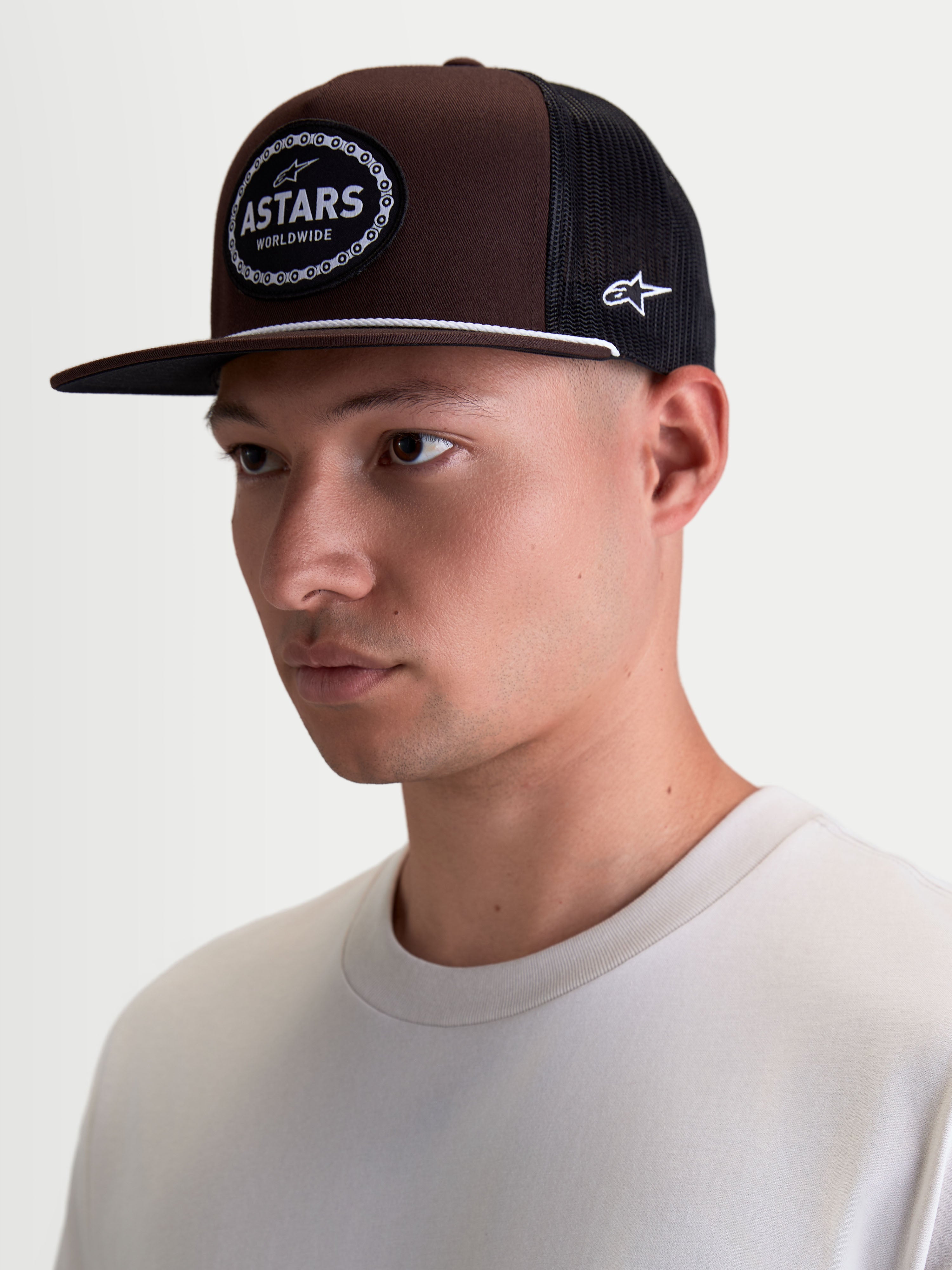 Alpinestars casquette trucker Hotlink, casquette sportswear marron et noire portée sur modèle, visière plate et couronne structurée en sergé, écusson Astars tissé avec bordure en chaîne de vélo