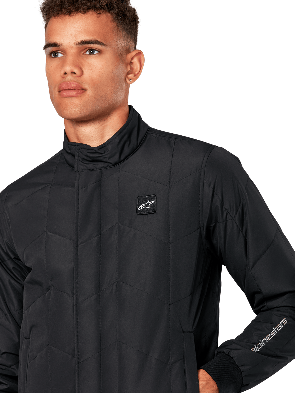 Veste Alpinestars Precedent, veste sportswear matelassée pour homme en noir, gros plan montrant le col bas, l'écusson du logo sur la poitrine et la broderie sur la manche, avec un motif matelassé en angle pour un look inspiré du sport automobile.