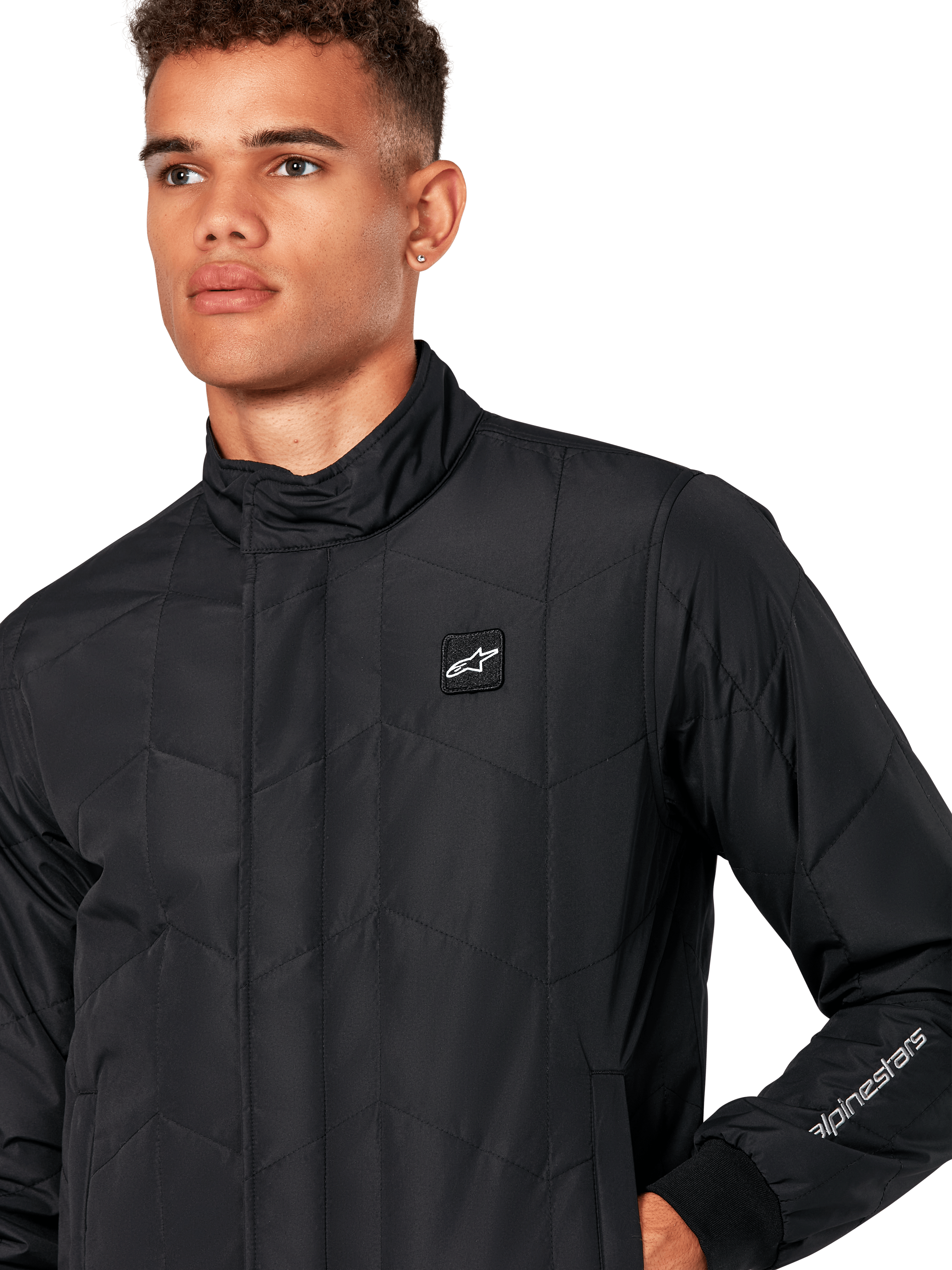 Veste Alpinestars Precedent, veste sportswear matelassée pour homme en noir, gros plan montrant le col bas, l'écusson du logo sur la poitrine et la broderie sur la manche, avec un motif matelassé en angle pour un look inspiré du sport automobile.