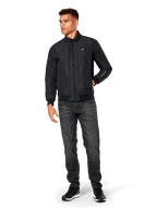 Veste Alpinestars Precedent, veste sportswear matelassée, noire, portée avec un jean gris foncé et des baskets noires, arborant un motif matelassé en angle, un col bas, des poignets et un ourlet en bords-côtes, avec un écusson logo blanc sur la poitrine et une broderie sur la manche.