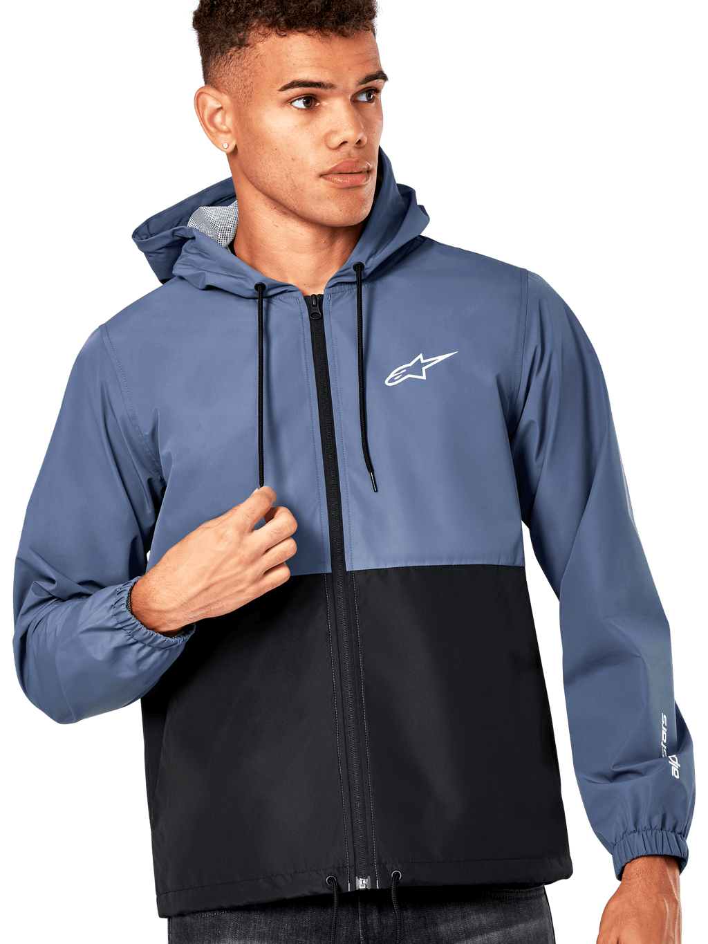 Modèle masculin portant la veste coupe-vent Alpinestars Speeder, design bicolore bleu ardoise et noir, capuche avec cordons de serrage noirs, logo blanc sur la poitrine, coupe-vent décontracté d'inspiration sport mécanique