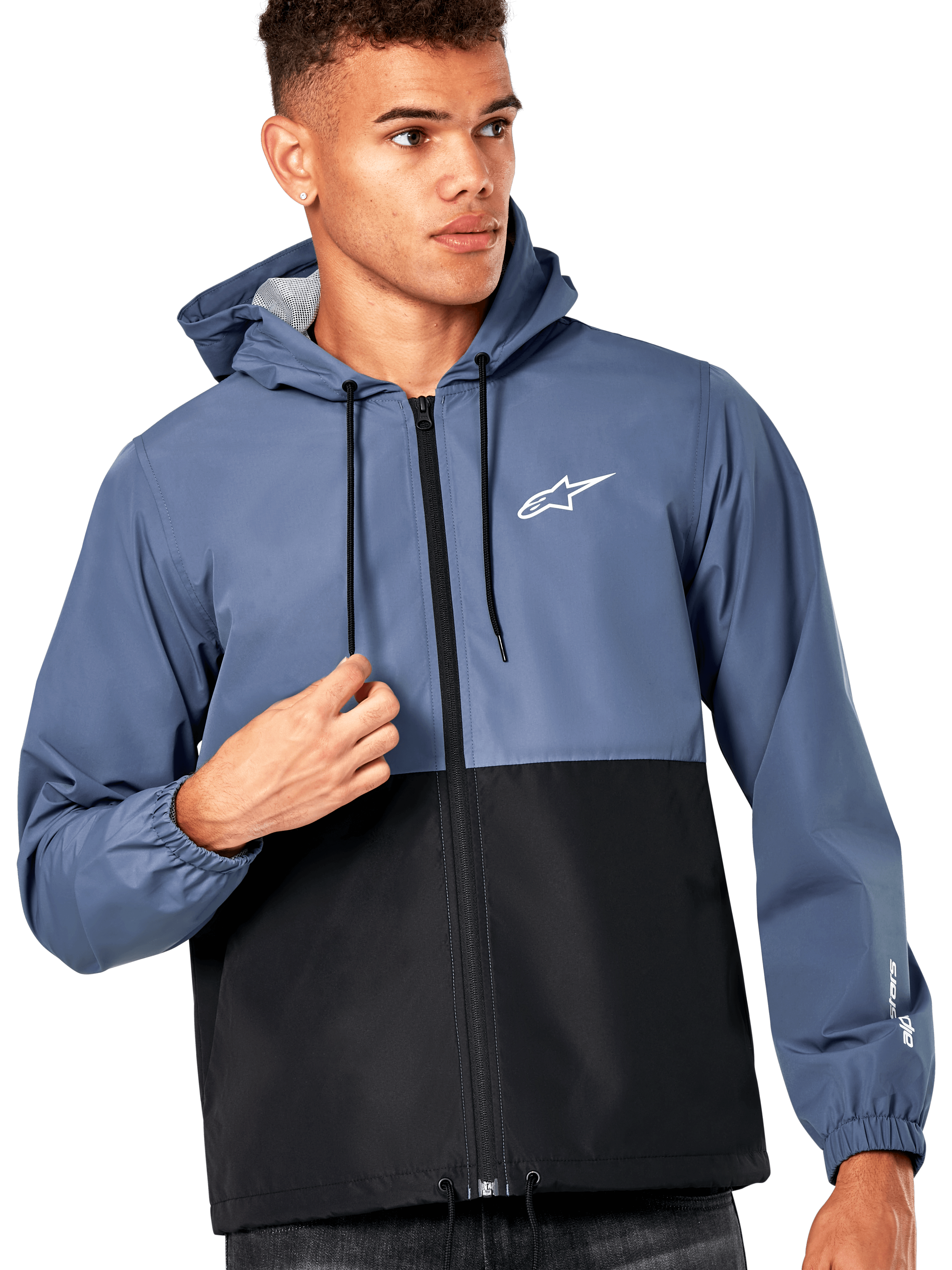 Modèle masculin portant la veste coupe-vent Alpinestars Speeder, design bicolore bleu ardoise et noir, capuche avec cordons de serrage noirs, logo blanc sur la poitrine, coupe-vent décontracté d'inspiration sport mécanique