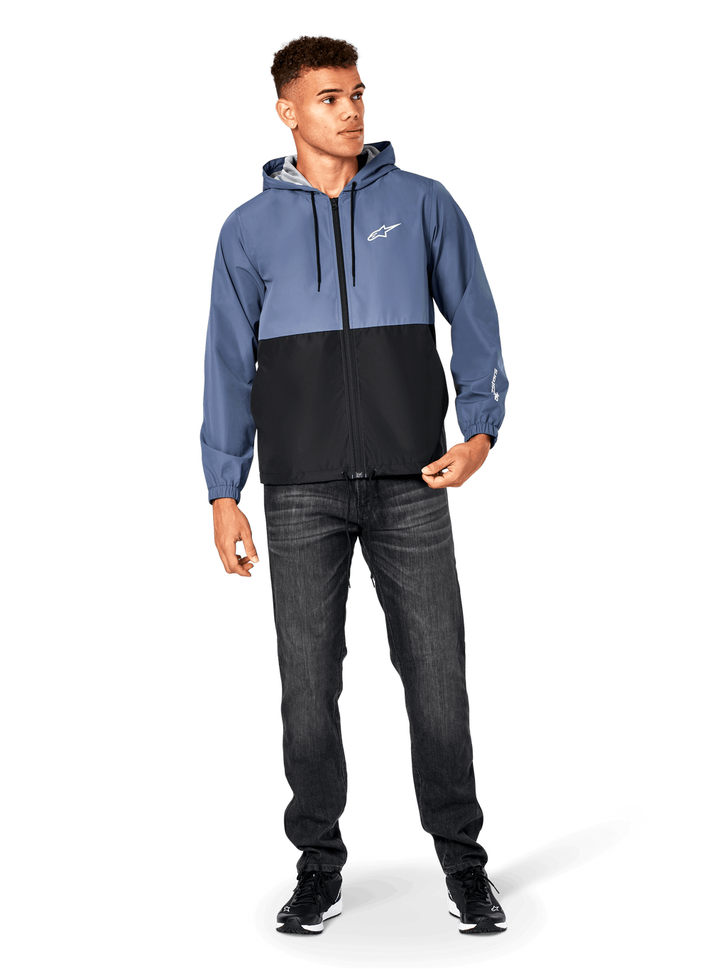 Veste coupe-vent Alpinestars Speeder, bleu ardoise et noir, veste légère à capuche avec doublure en mesh, logo étoile blanc sur la poitrine, portée avec un jean noir et des baskets, design casual motorsport streetwear