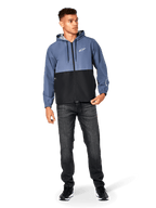 Veste coupe-vent Alpinestars Speeder, bleu ardoise et noir, veste légère à capuche avec doublure en mesh, logo étoile blanc sur la poitrine, portée avec un jean noir et des baskets, design casual motorsport streetwear