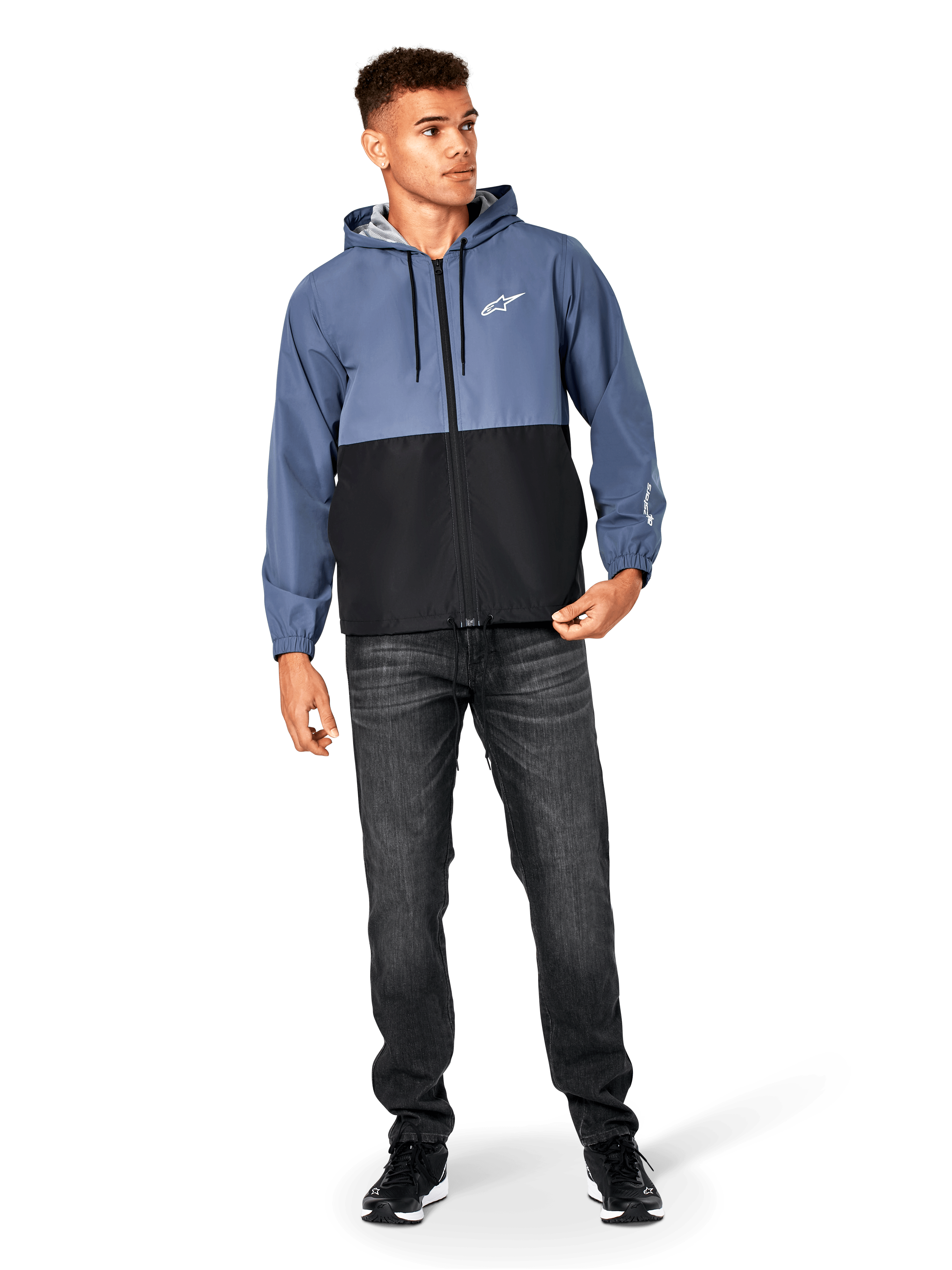 Veste coupe-vent Alpinestars Speeder, bleu ardoise et noir, veste légère à capuche avec doublure en mesh, logo étoile blanc sur la poitrine, portée avec un jean noir et des baskets, design casual motorsport streetwear