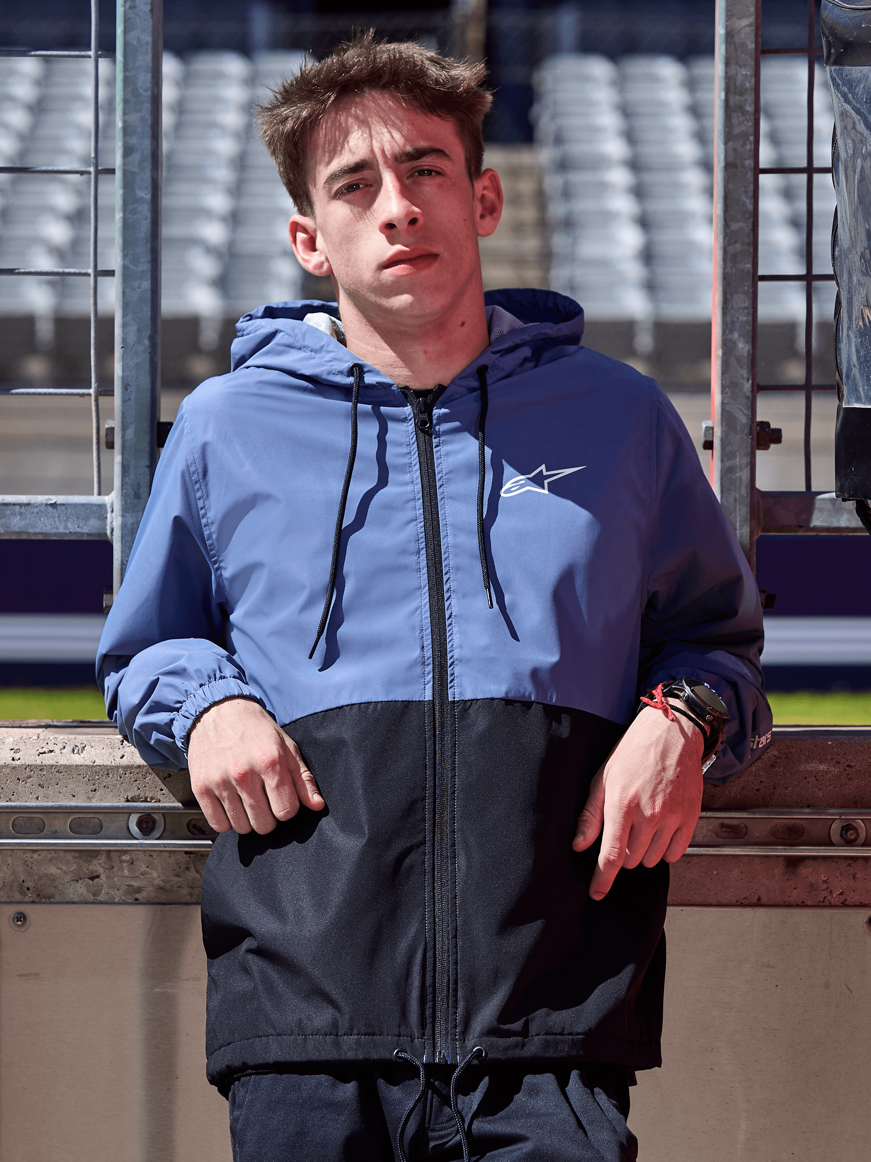 Veste coupe-vent Alpinestars Speeder, bleu ardoise et noir, coupe-vent à capuche avec design bicolore, logo blanc sur la poitrine, vêtement lifestyle décontracté porté sur un circuit de course