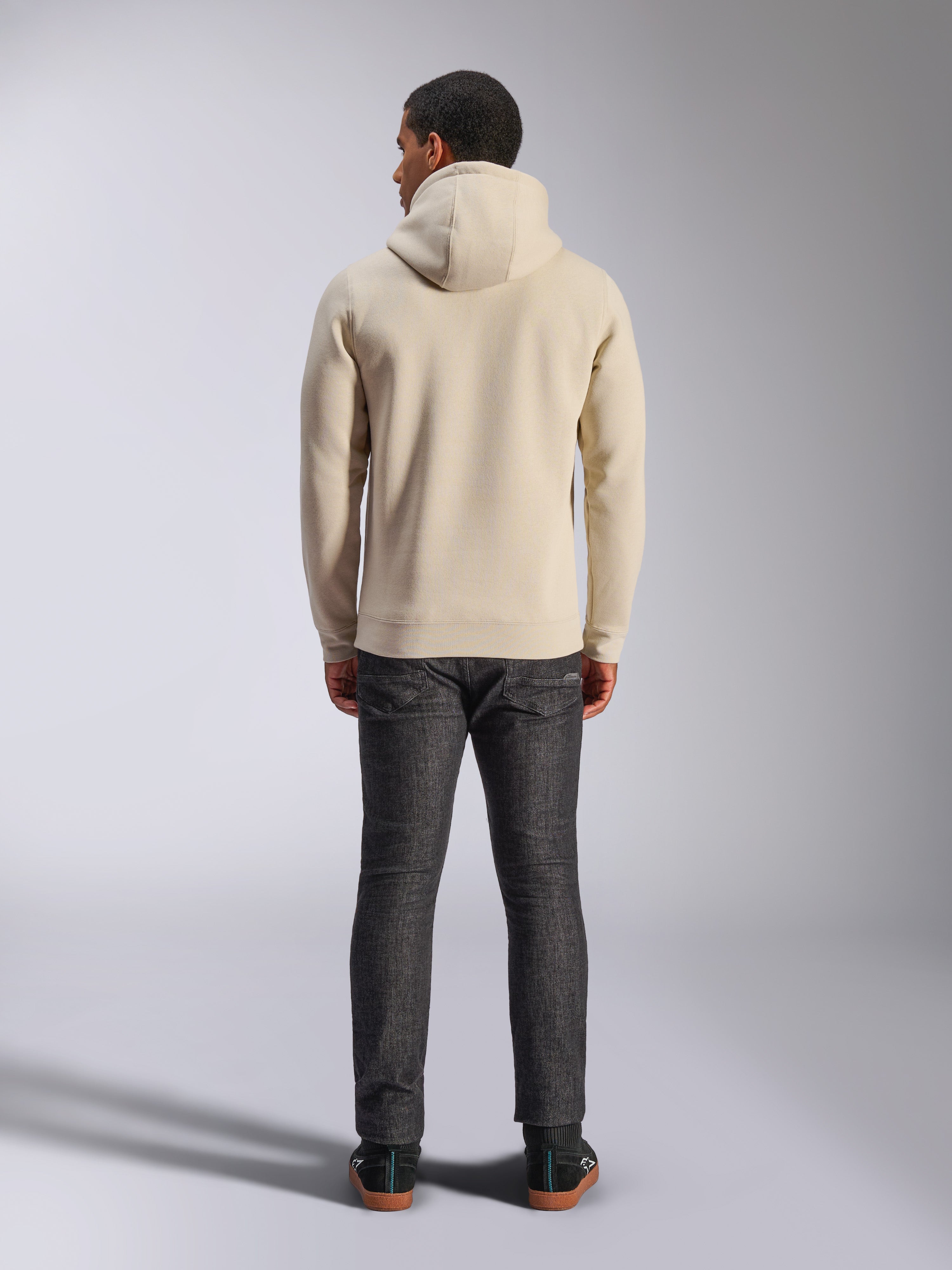 Sweat à capuche Alpinestars Ageless V3, vue de dos, sweat-shirt à capuche blanc cassé, vêtement lifestyle décontracté, porté avec un jean gris foncé, ourlet et poignets côtelés, design épuré et minimaliste
