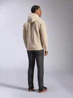 Sweat à capuche Alpinestars Ageless V3, sweat décontracté en polaire blanc cassé vu de dos, avec poignets et ourlet côtelés, porté avec un jean slim foncé et des baskets Alpinestars noires