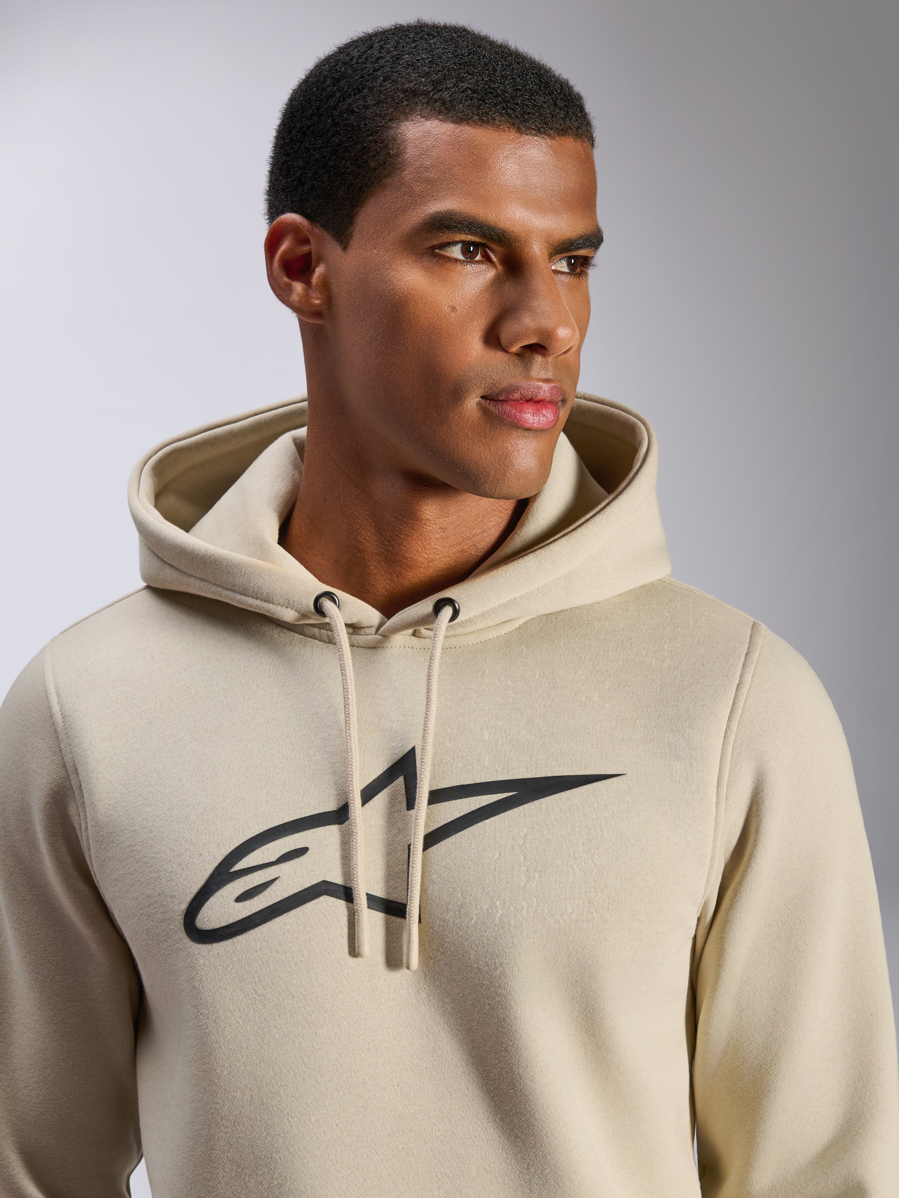 Sweat à capuche Alpinestars Ageless V3, sportswear décontracté, blanc cassé avec logo étoile Alpinestars brodé noir, capuche avec cordon de serrage, vue rapprochée sur mannequin, polaire douce, design moderne inspiré du sport automobile