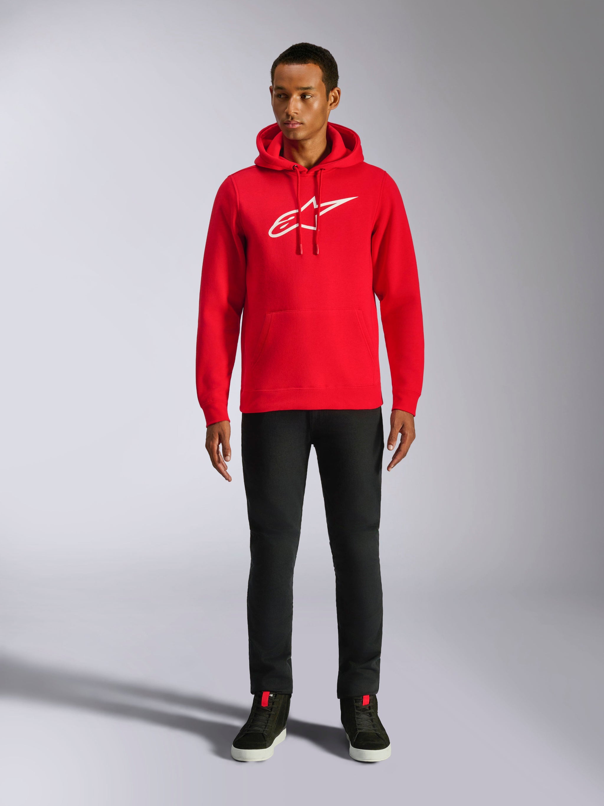 Sweat à capuche Alpinestars Ageless V3, streetwear décontracté, rouge avec logo Alpinestars brodé en blanc, porté par un mannequin homme avec un pantalon noir, capuche à cordon de serrage, poche kangourou à l'avant, design moderne inspiré du sport automobile