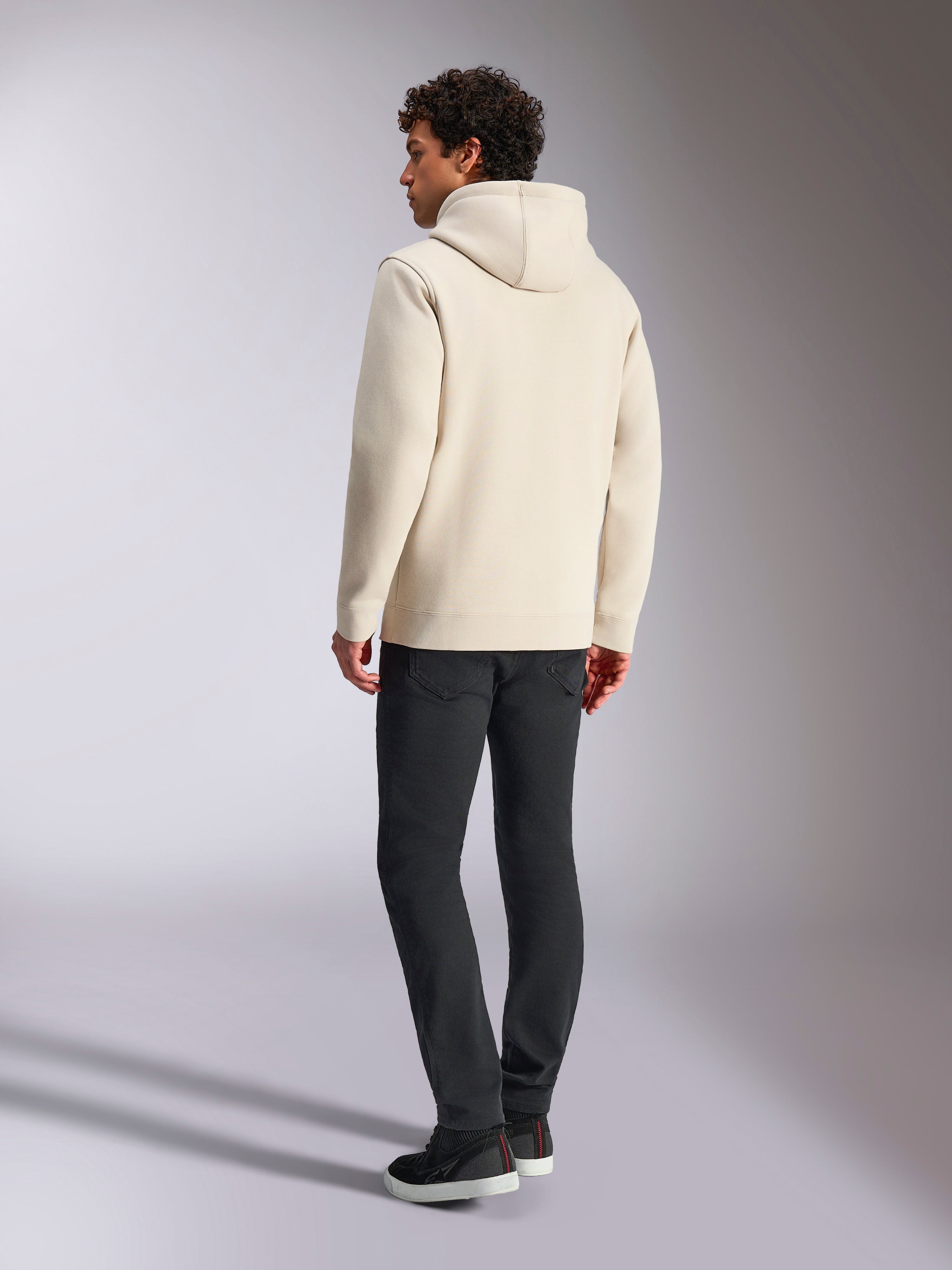 Sweat à capuche Alpinestars Always V3, blanc cassé, vue arrière d'un mannequin portant le sweat à capuche et un pantalon noir, streetwear décontracté inspiré du sport automobile, design minimaliste avec capuche et ourlet côtelé