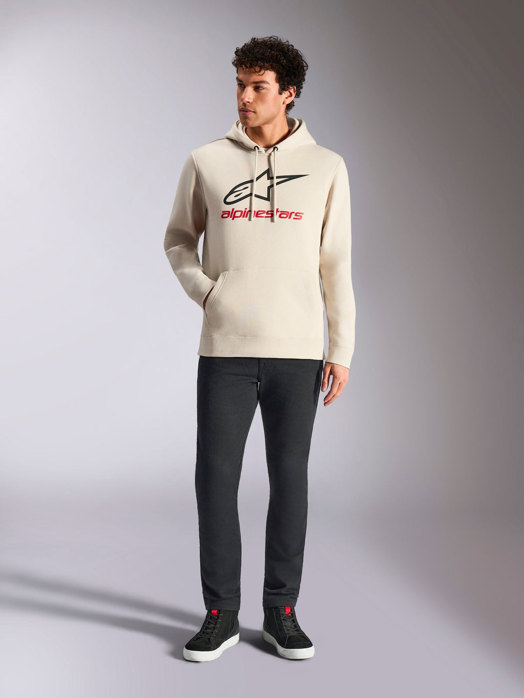 Alpinestars Always V3 Hoodie, streetwear décontracté, blanc cassé avec logo étoile noir et lettrage rouge, capuche à cordon de serrage, manches longues, porté par un mannequin homme avec pantalon noir et baskets noires