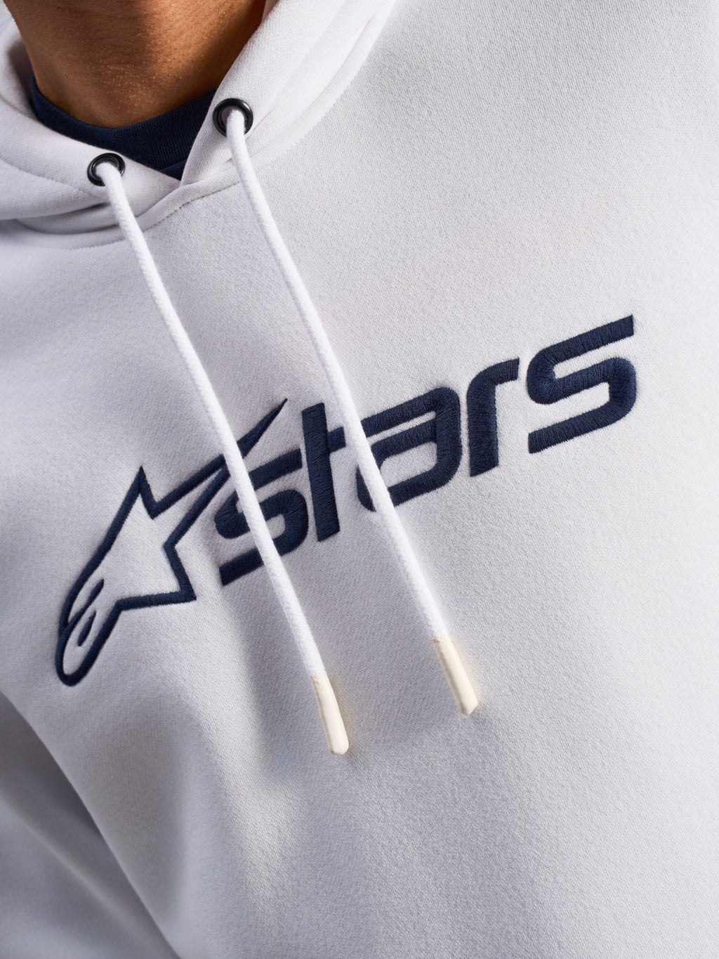 Sweat à capuche Alpinestars Blaze V3, blanc et bleu marine, gros plan sur la poitrine avec logo imprimé bleu marine à l'avant et cordons de serrage blancs à embouts trempés, vêtement streetwear décontracté motorsport