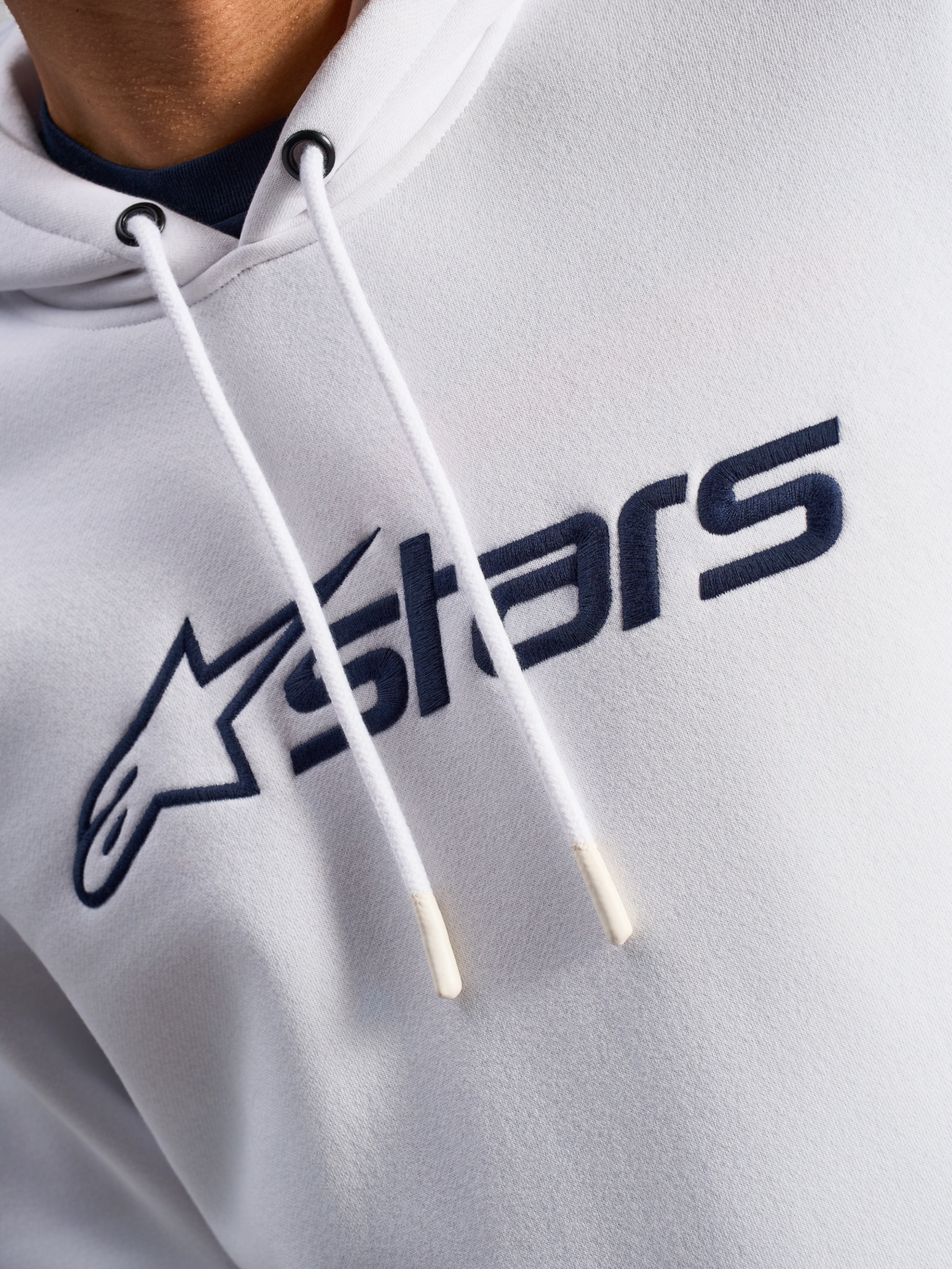Sweat à capuche Alpinestars Blaze V3, blanc et bleu marine, gros plan sur la poitrine avec logo imprimé bleu marine à l'avant et cordons de serrage blancs à embouts trempés, vêtement streetwear décontracté motorsport
